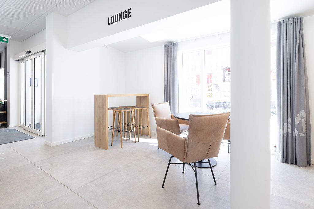 A modern lounge area with a round table and chairs, a wooden partition, and a view of the city through large windows.