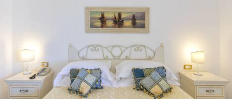 A neatly made bed with patterned bedding, two bedside tables with lamps, and a painting above the bed.