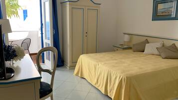 Habitación de hotel con cama, escritorio con silla, armario y ventana con cortinas.