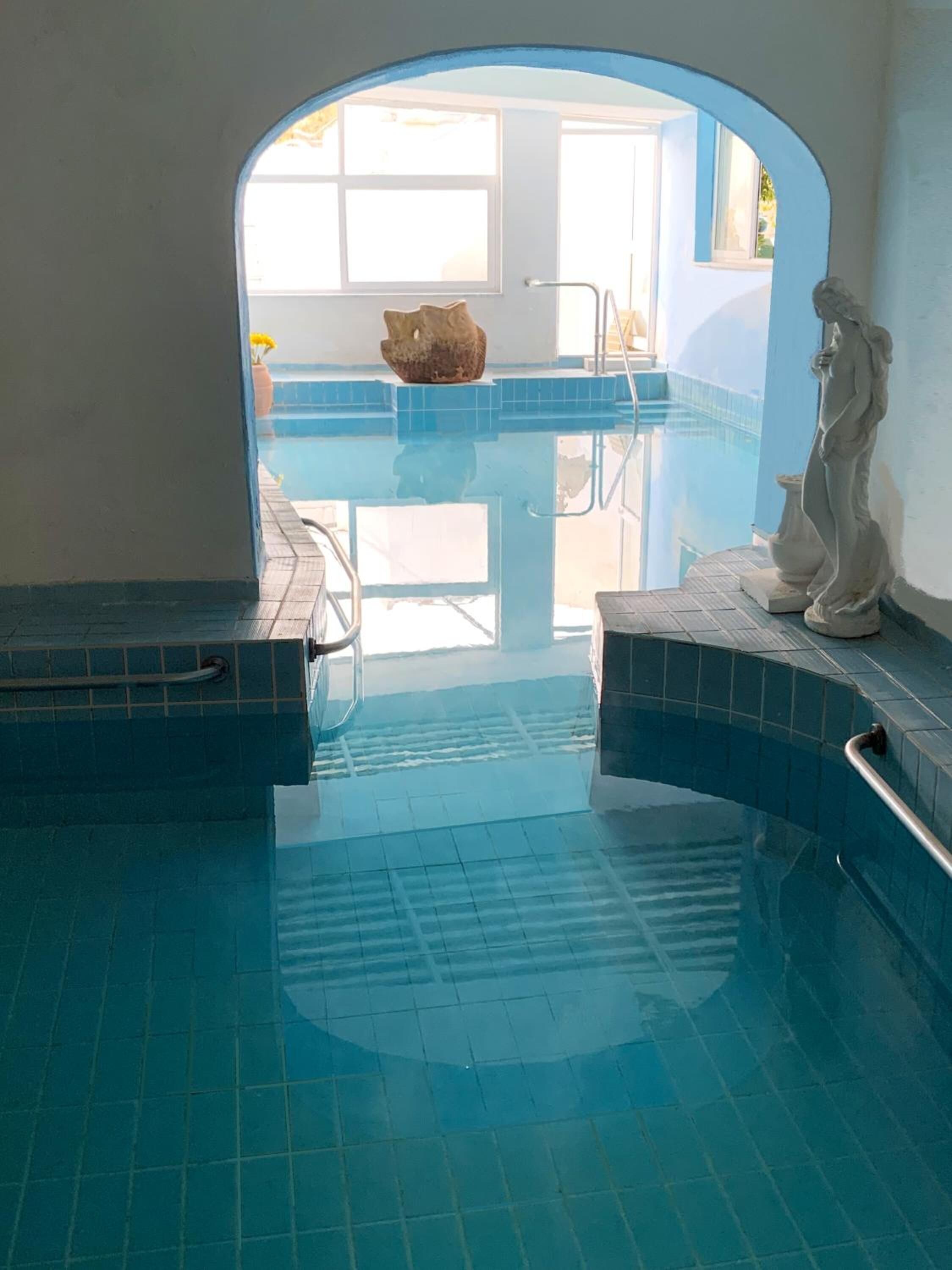 A swimming pool with a clear view of the outside, a stone sculpture, and a tiled floor.