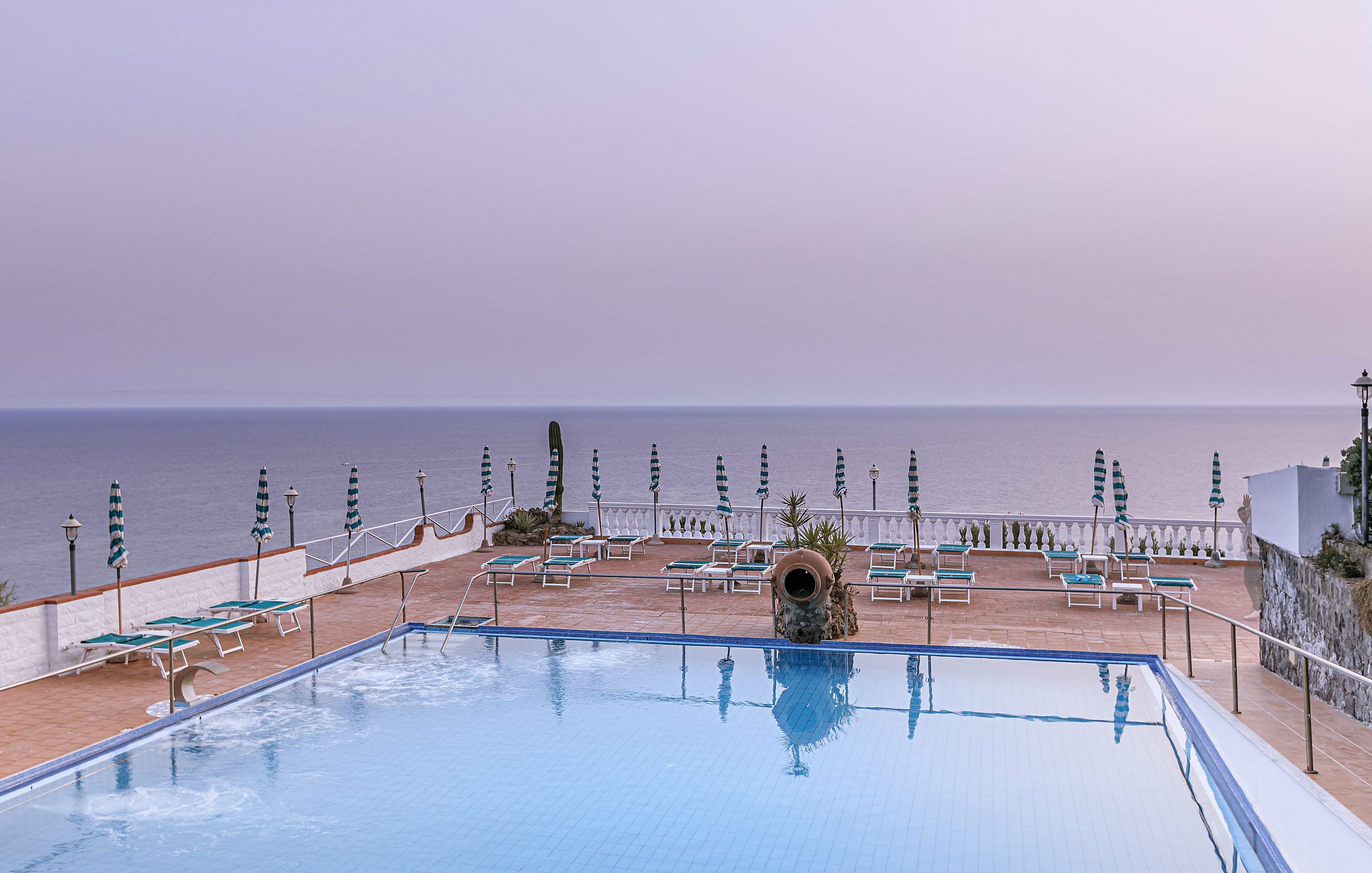 Un espace piscine doté de chaises longues et de parasols, avec vue sur la mer.