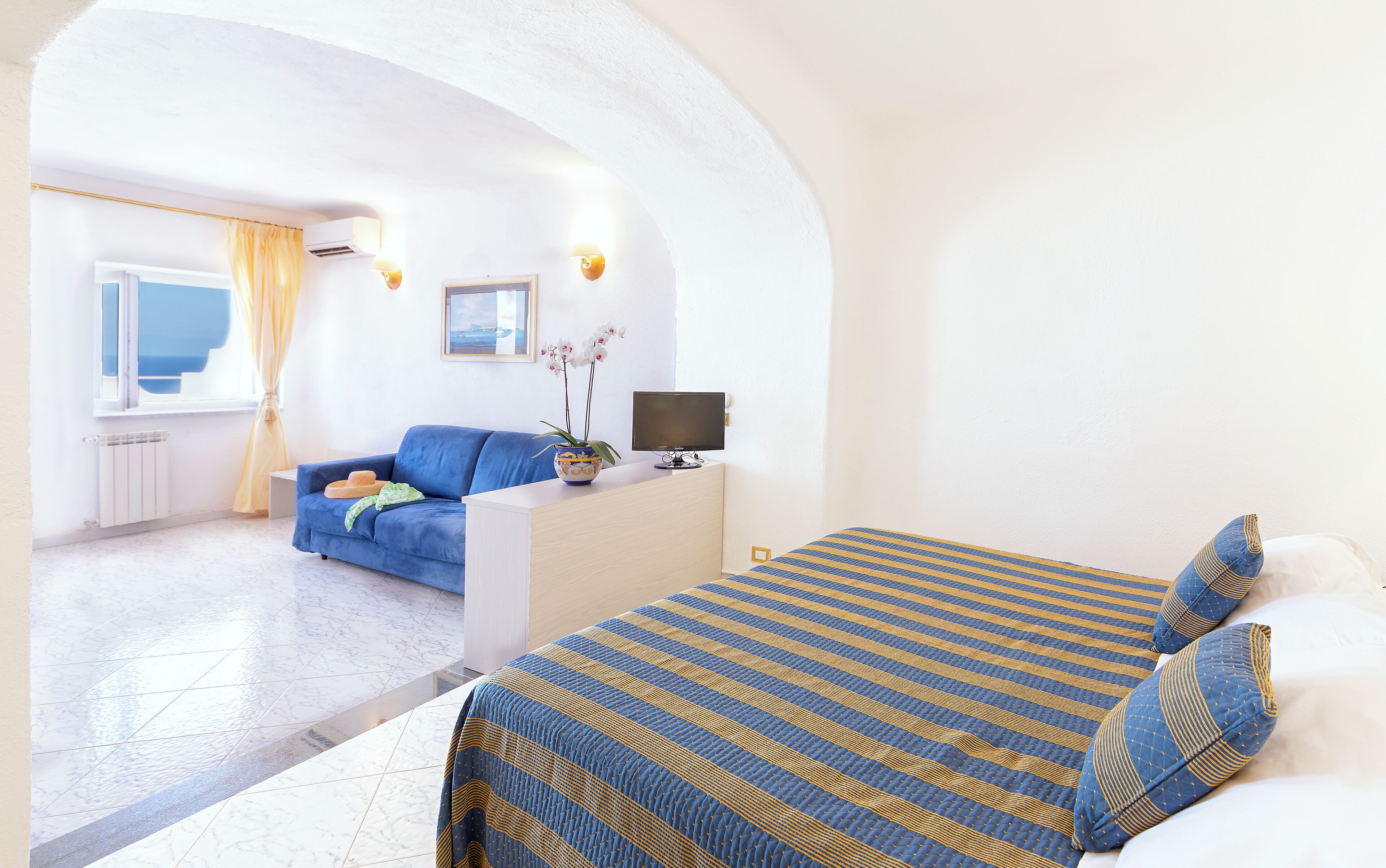 A hotel room with a bed, a sofa, a TV, and a window with curtains.