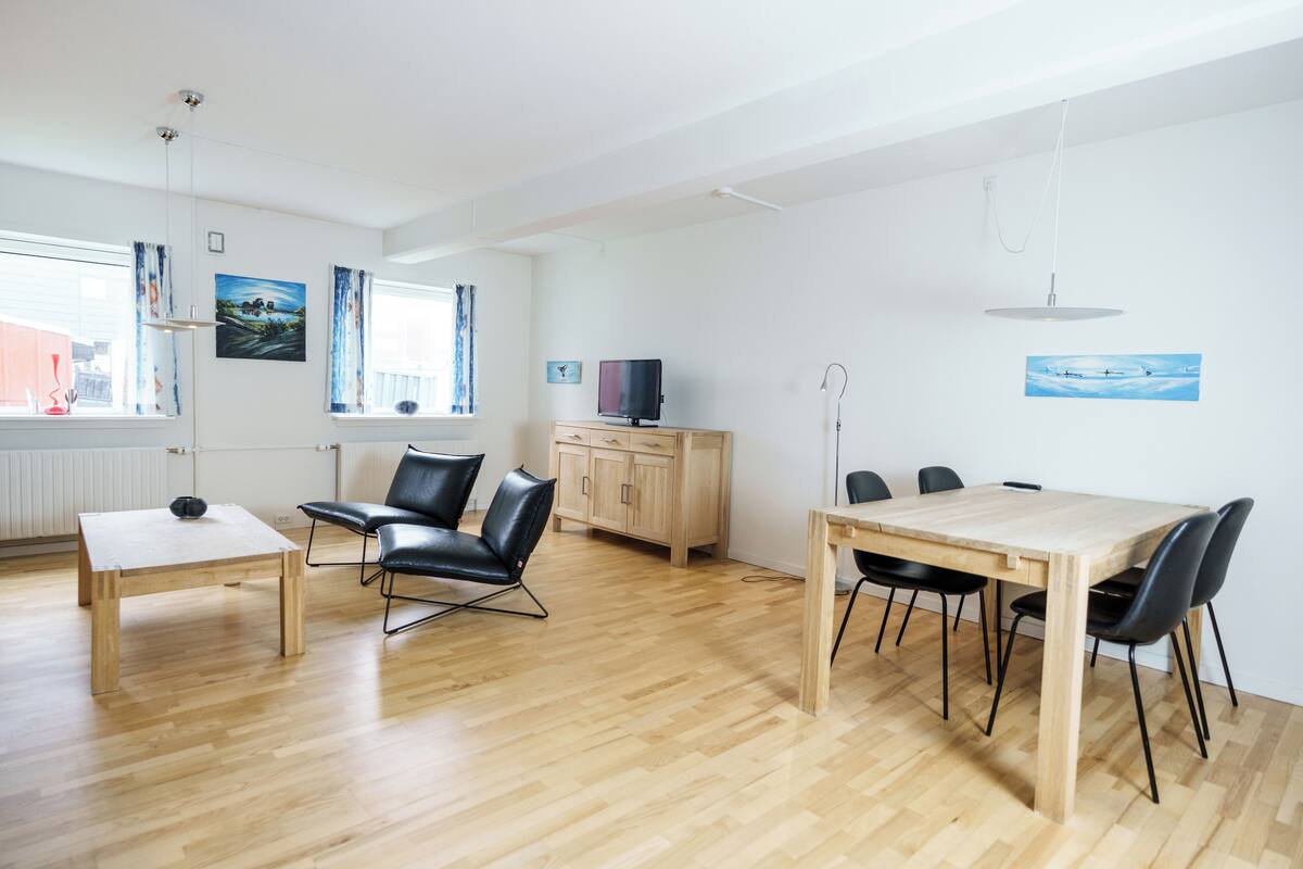 A modern living room with a wooden dining table, black chairs, a TV, and a cabinet.