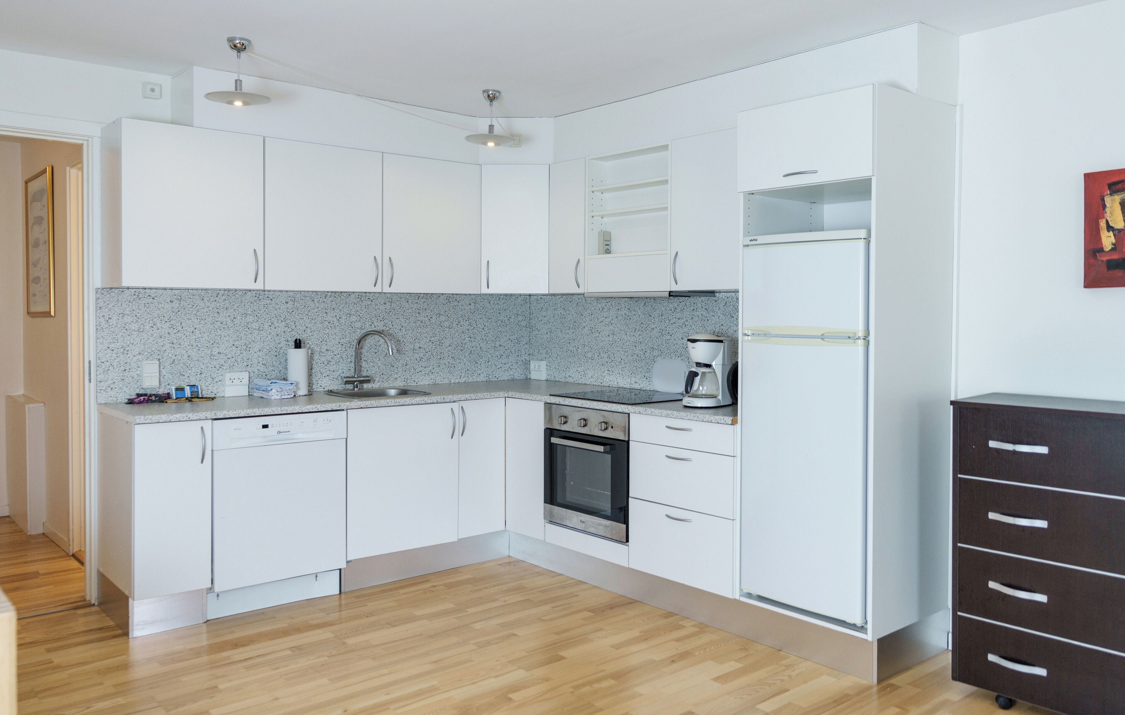 A modern kitchen with white cabinets, a granite countertop, an oven, and a coffee maker.