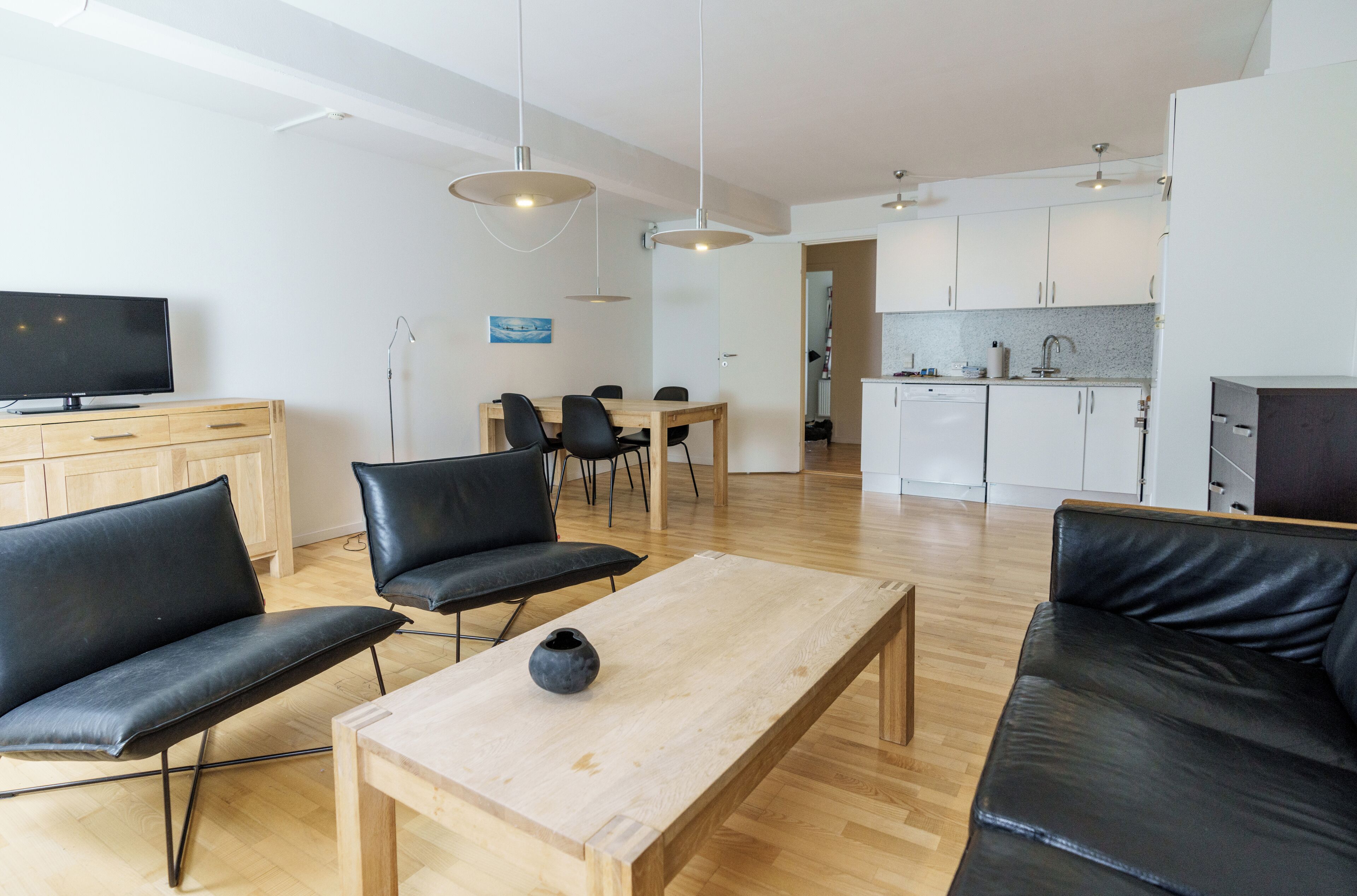 Una sala de estar moderna con una mesa de centro de madera, sofás de cuero negro y un televisor sobre un mueble de madera.