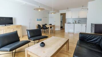 Una sala de estar moderna con una mesa de centro de madera, sofás de cuero negro y un televisor sobre un mueble de madera.