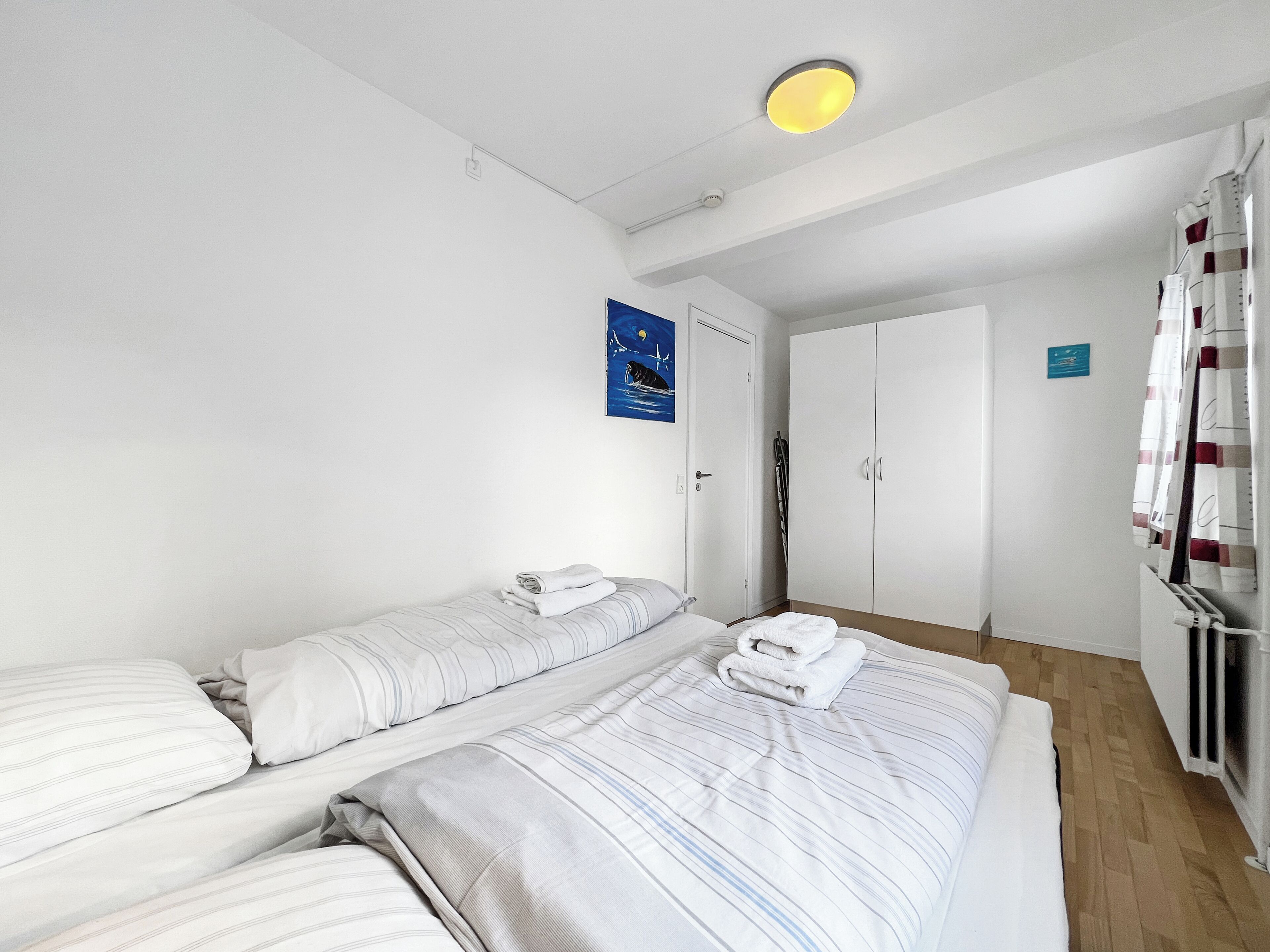 A hotel room with two beds, a wardrobe, a radiator, and a poster on the wall.
