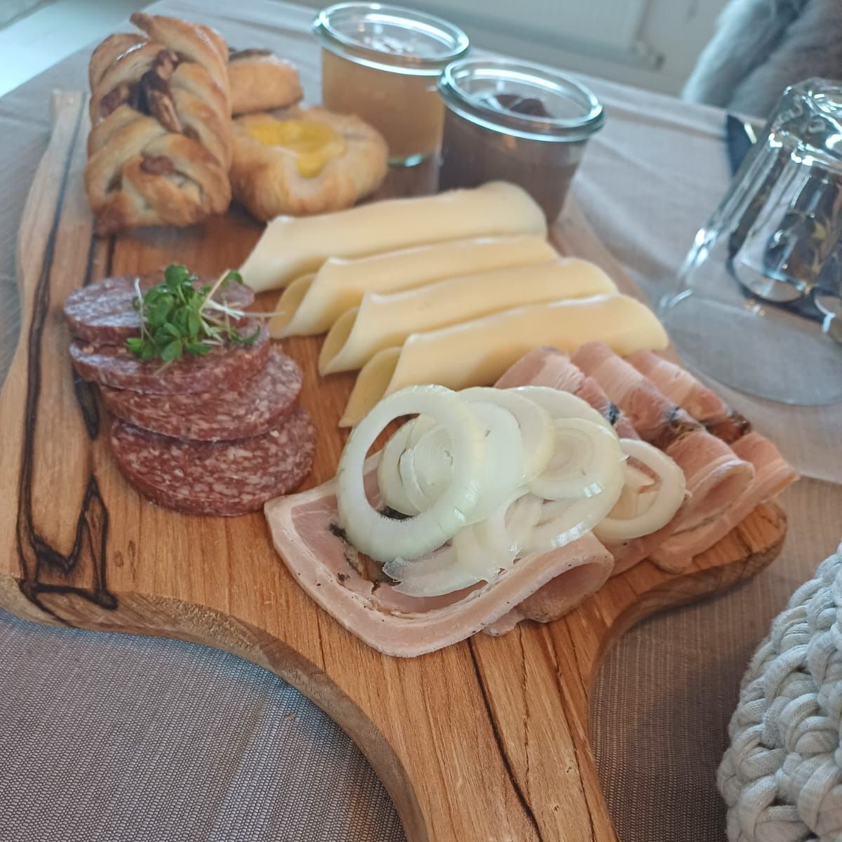 Ein Holzbrett mit verschiedenen Speisen, darunter Wurst, Käse und eingelegtes Gemüse.