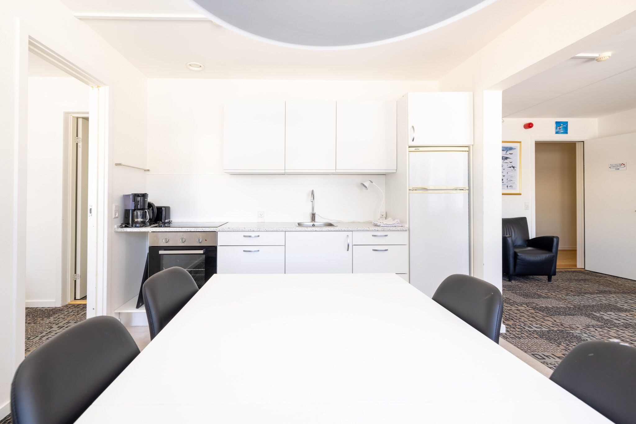 A modern kitchen with white cabinets, a sink, and a stove. There is a dining table with four chairs in the foreground.