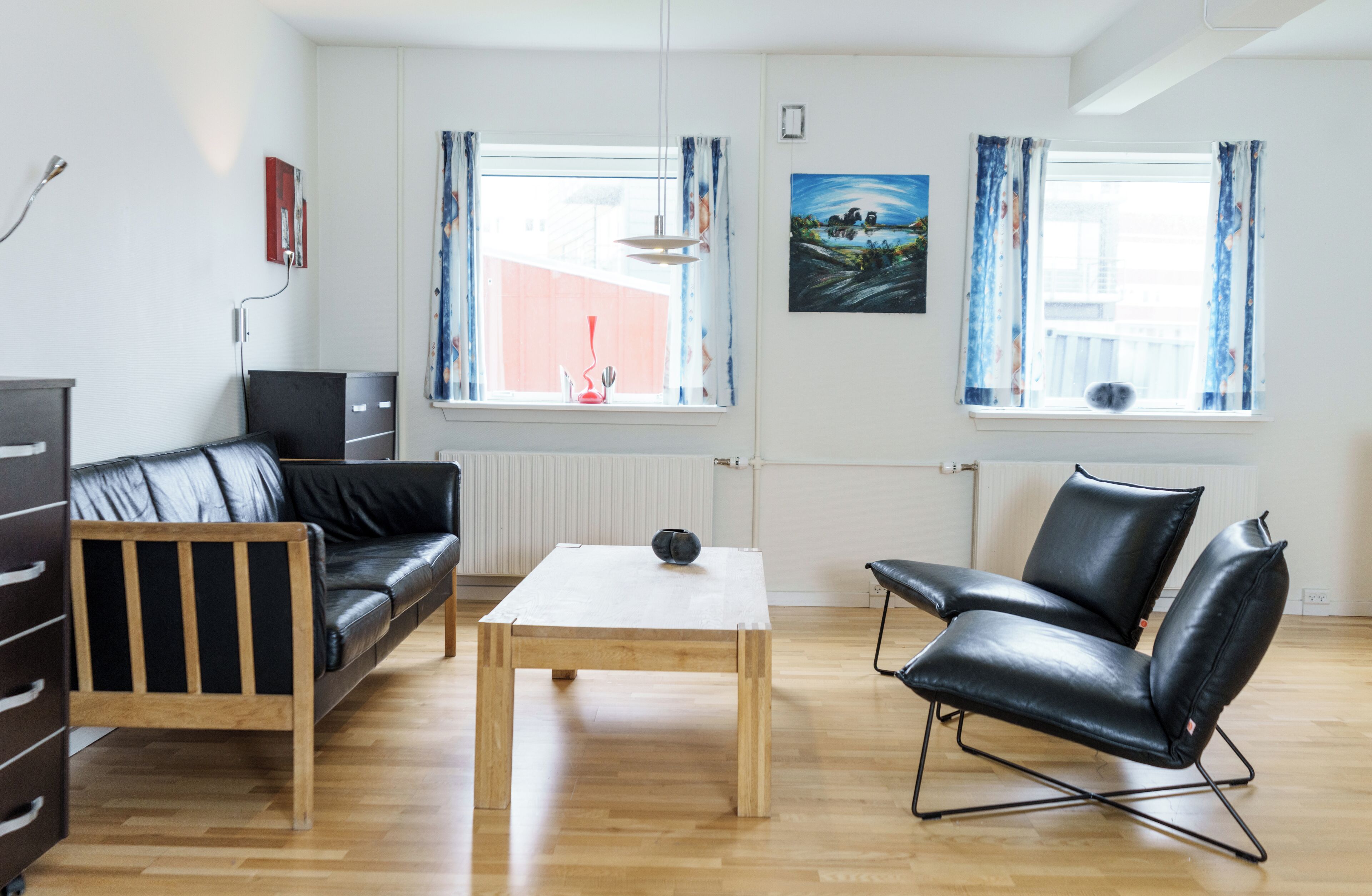 Una sala de estar moderna con una mesa de centro de madera, un sofá de cuero negro, un sillón de cuero negro y un mueble de televisión negro.