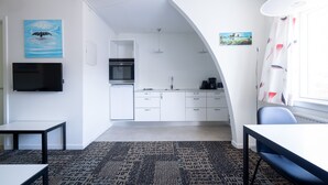 A modern kitchen with white cabinets, a black refrigerator, and a built-in oven. There is a dining area with a table and chairs, and a TV mounted on the wall. - Hotel Nordbo City (Nuuk)