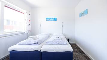 Een hotelkamer met twee enkele bedden, een raam met gordijnen, een radiator en een klein tafeltje.