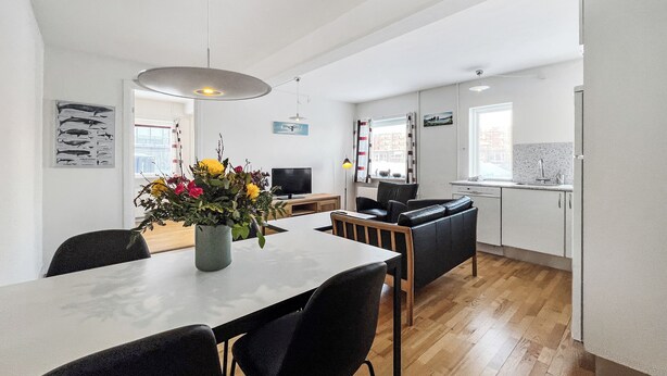 A modern kitchen with a dining area, wooden flooring, and a vase of flowers on the table. - Hotel Nordbo City (Nuuk)