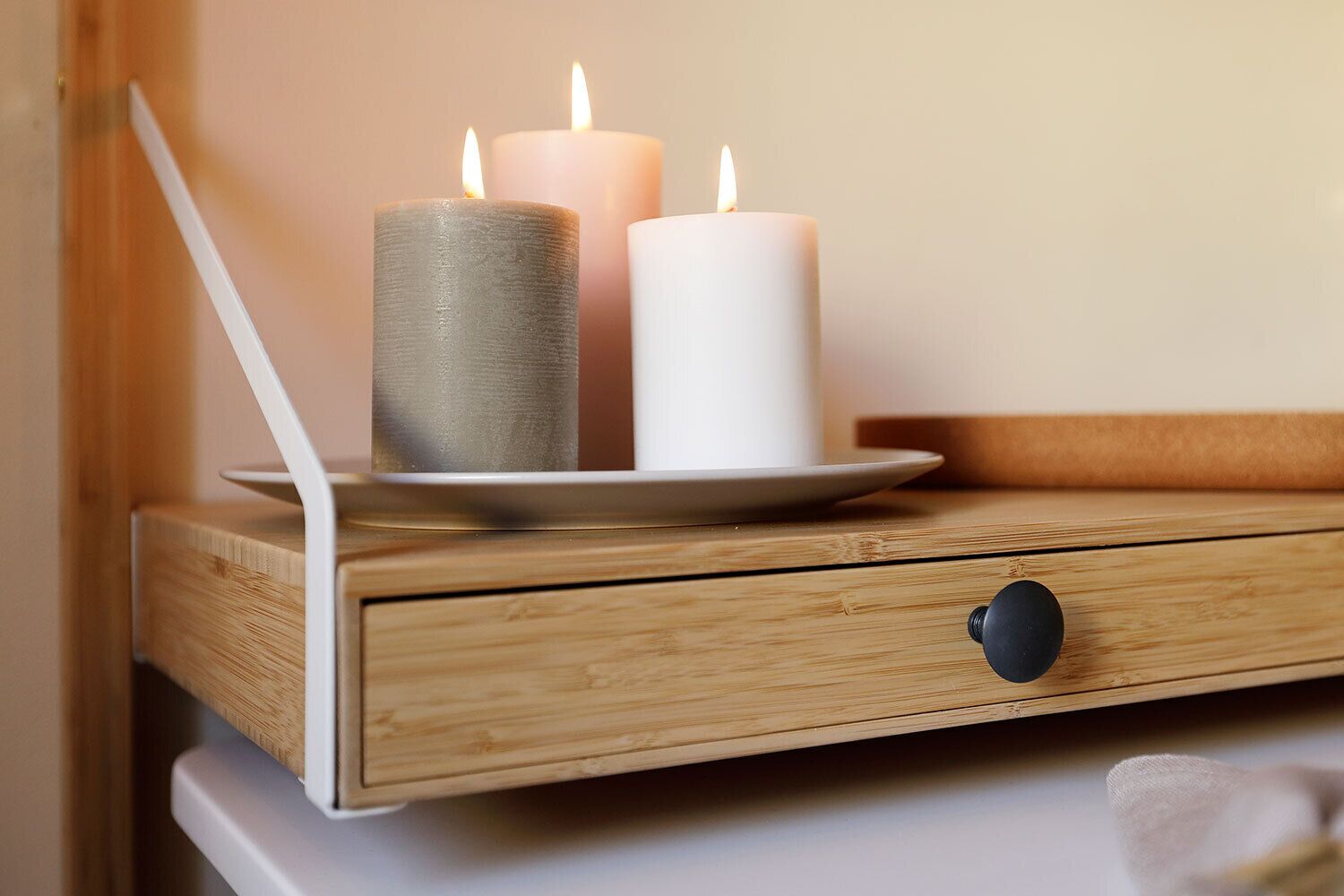 A wooden bedside table with three candles, a white plate, and a black object on it.