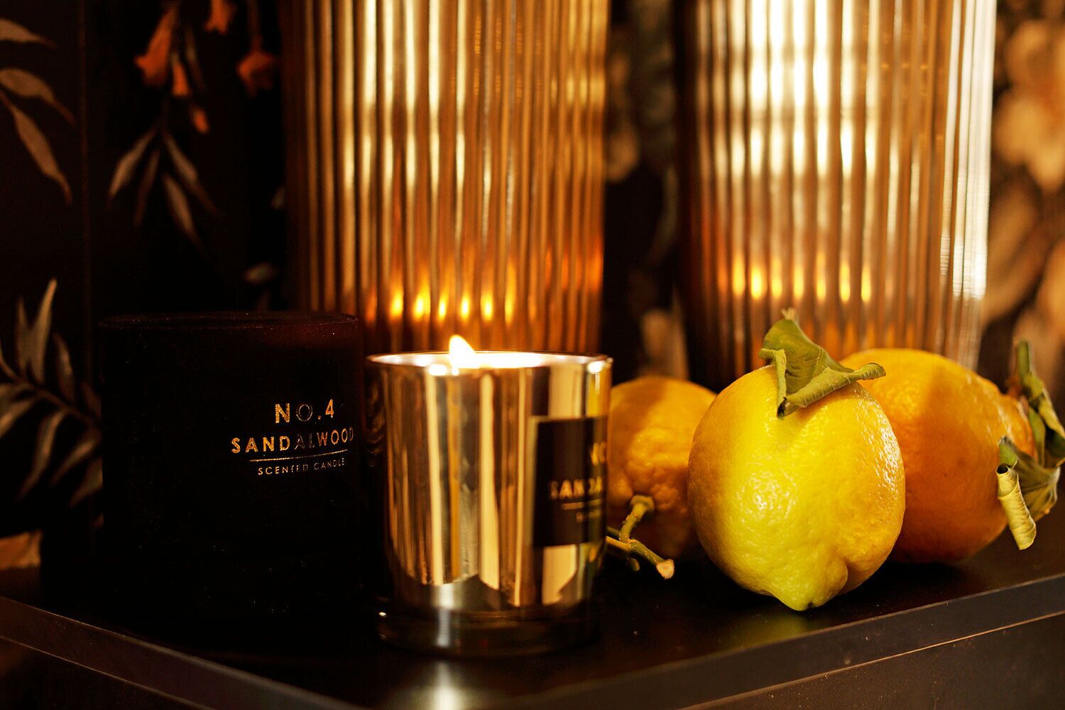 A candle, a scented candle, and lemons on a table.