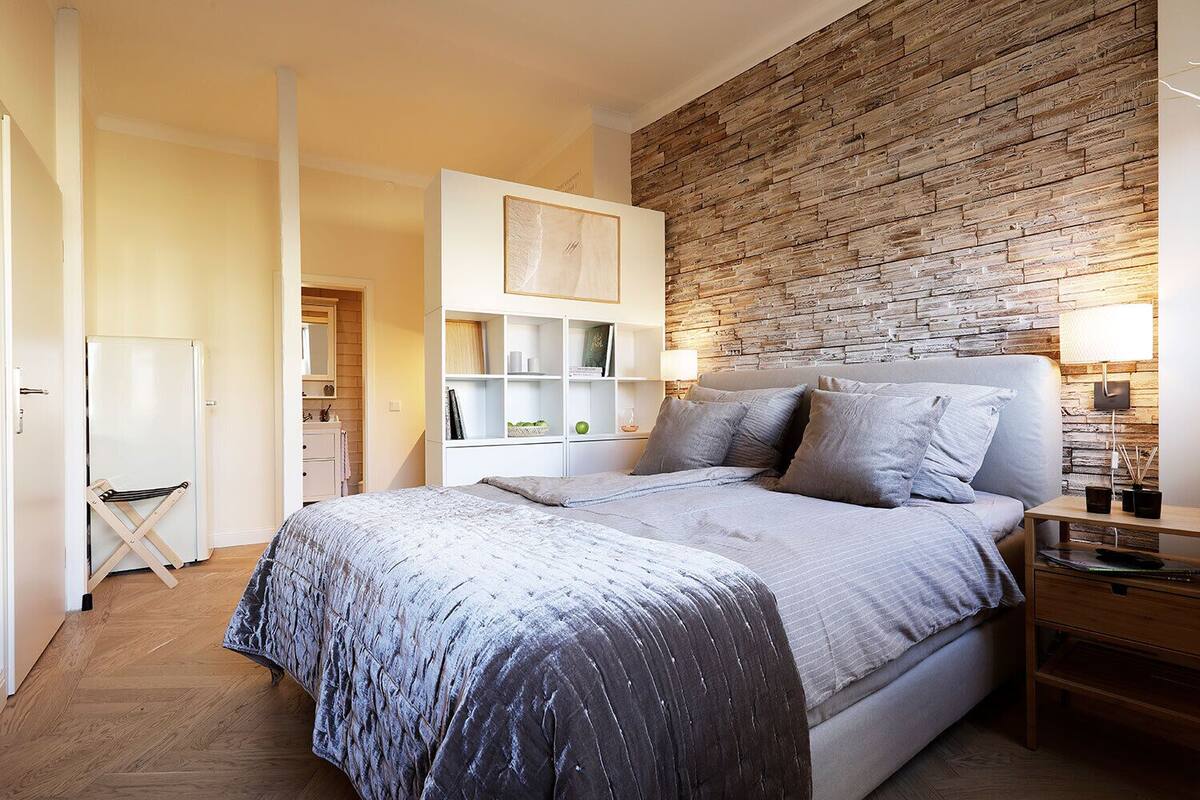 A bedroom with a bed, bedside tables, a wardrobe, and a brick-patterned wall.