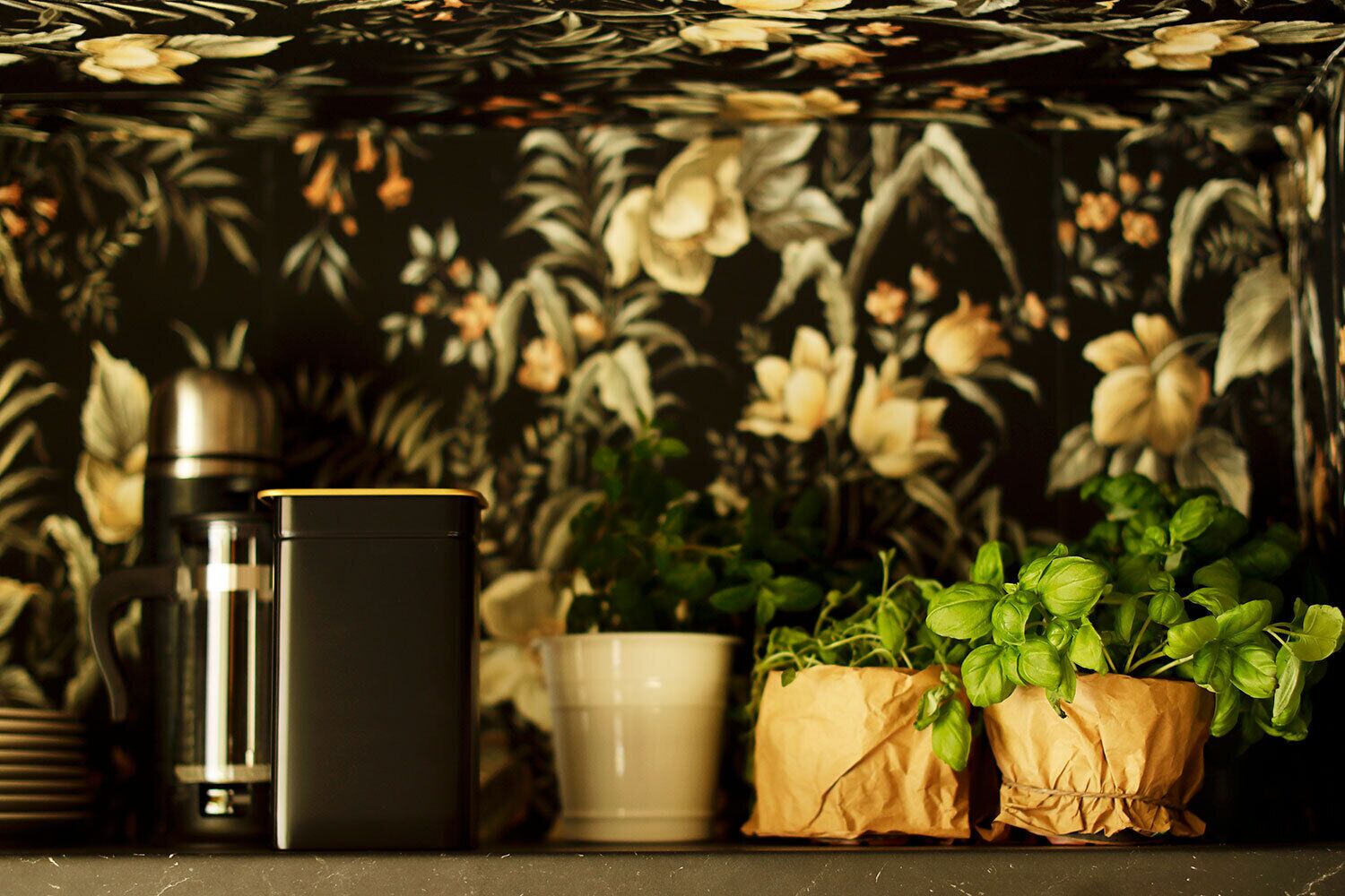 A shelf with a thermos, a black container, a white mug, and two potted plants.