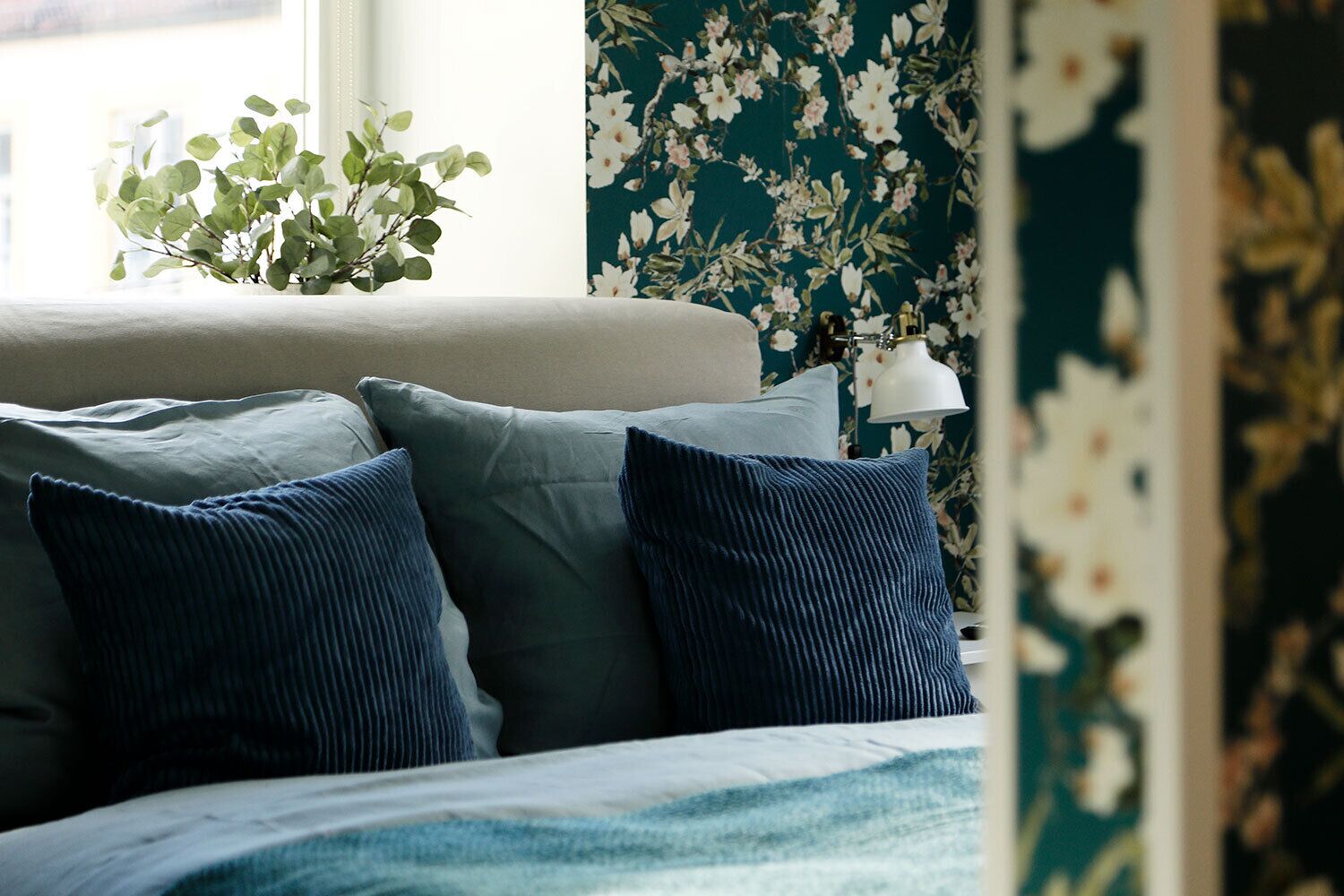 Een bed met blauwe kussens, een witte lamp en bloemenbehang.