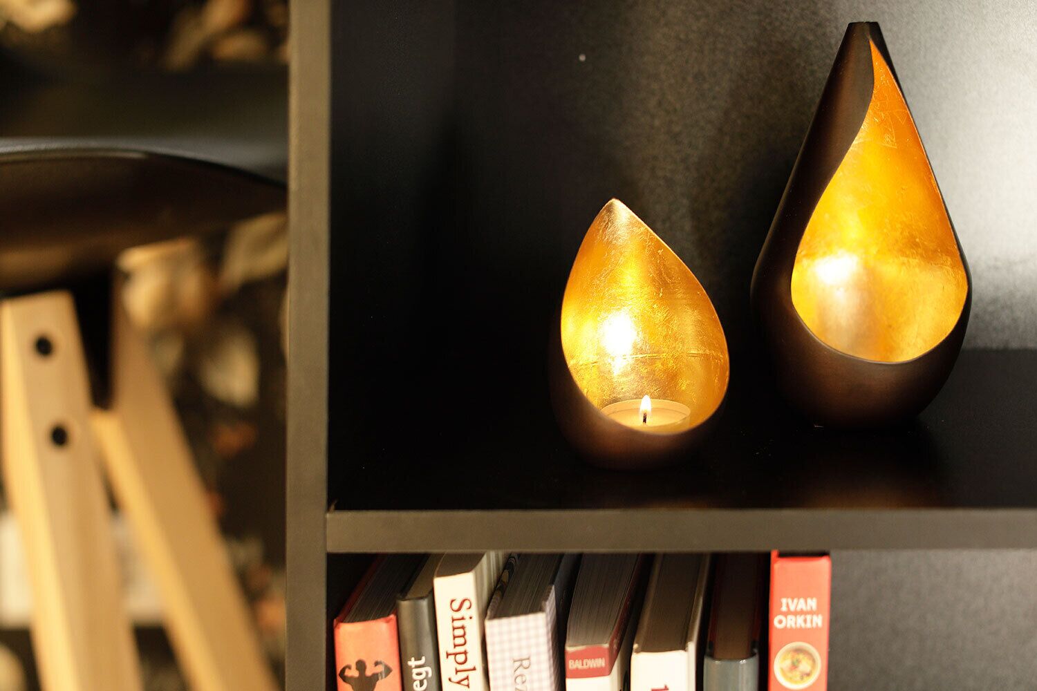 Deux chandeliers en forme de goutte d’eau sont posés sur une étagère, avec des livres en dessous.