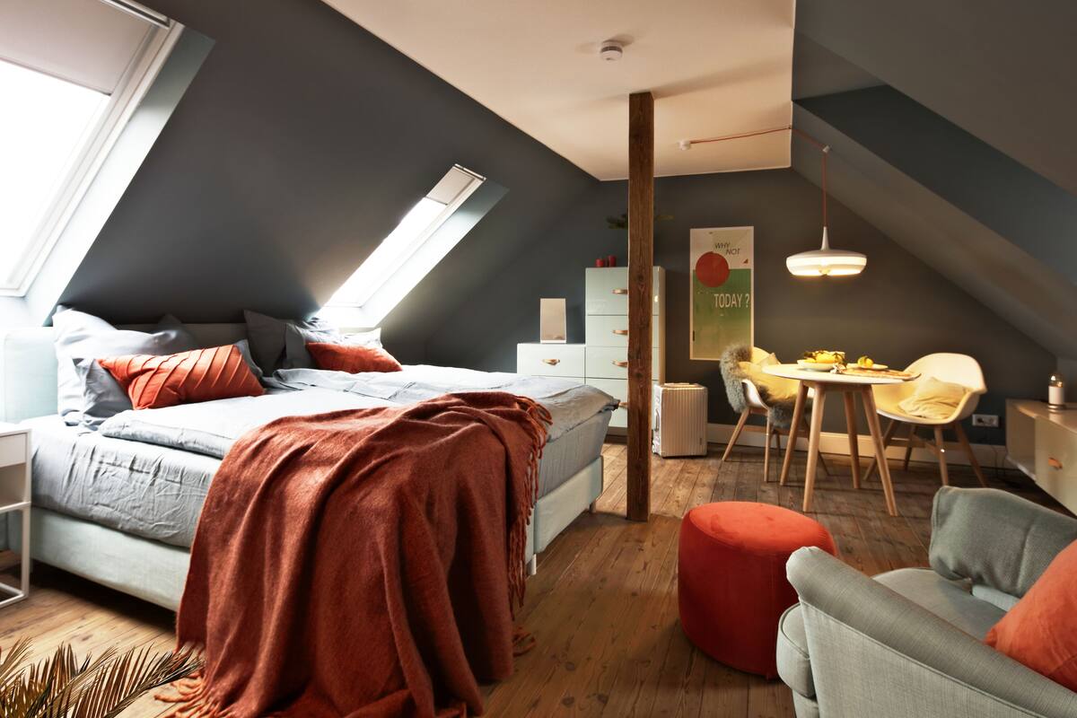 A modern bedroom with a loft-style bed, a dining area, and a small kitchenette.