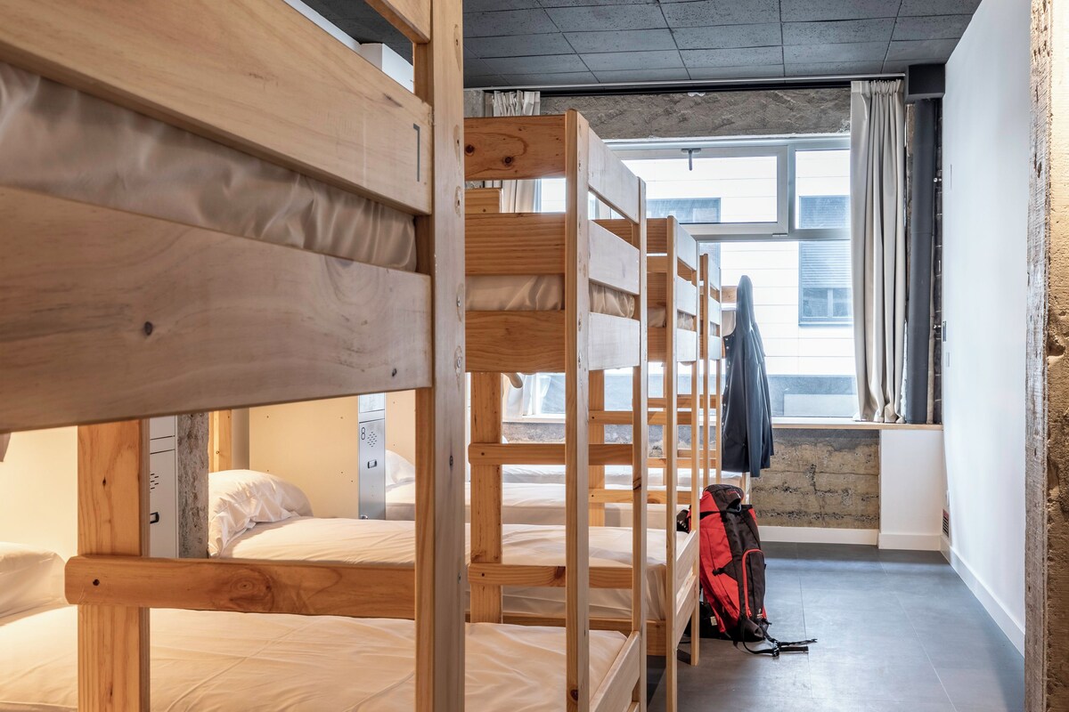 A dormitory room with bunk beds, a window with curtains, and a backpack on the floor.