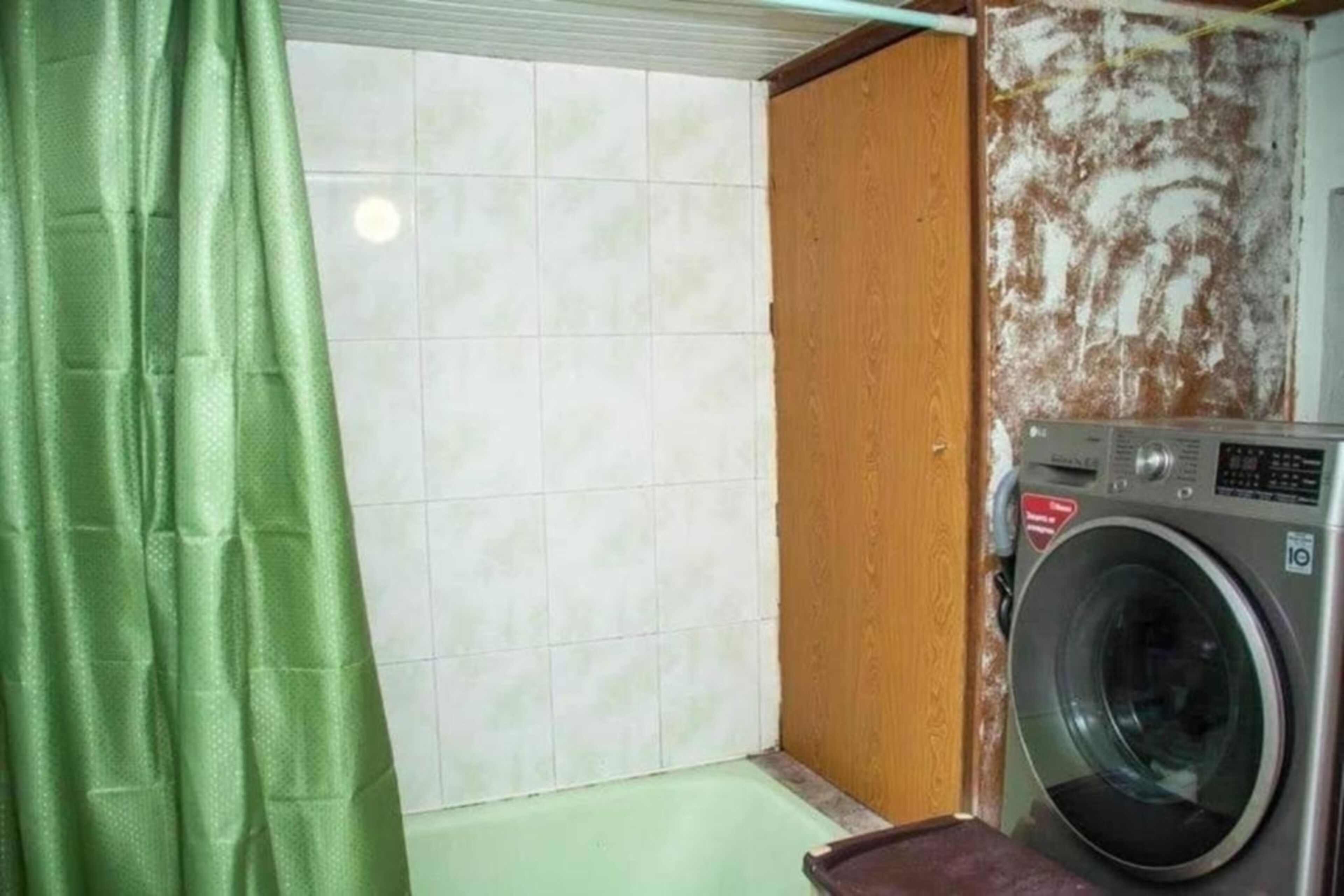 A small laundry room with a washing machine, a green curtain, and a tiled wall.