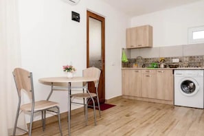 A compact kitchen with a washing machine, wooden cabinets, and a dining area with two chairs and a table. - Guest House Beautiful Tbilisi (Tbilisi)