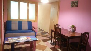 Une petite pièce agréable et chaleureuse, avec un canapé, une table à manger et des chaises, et un sol carrelé.