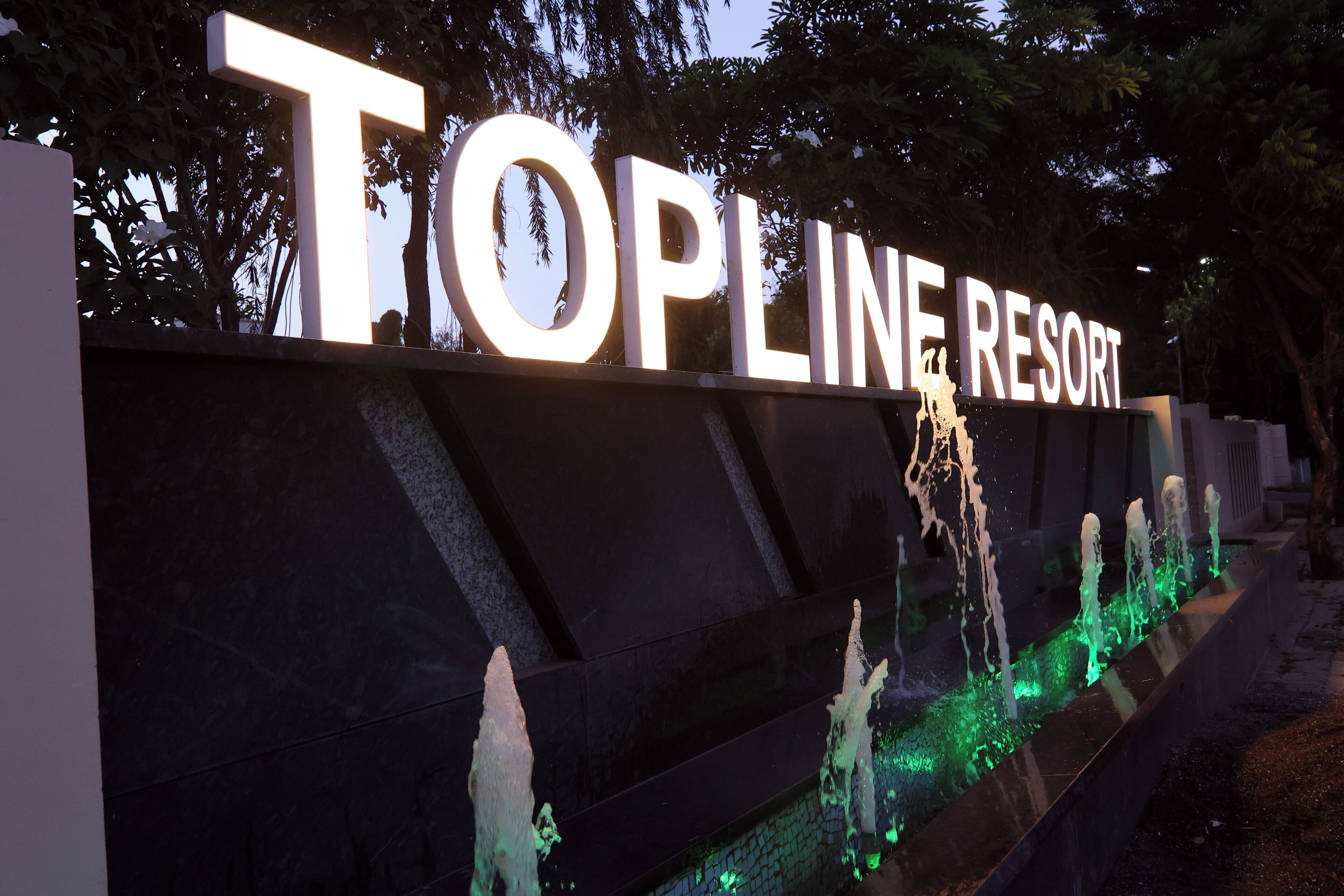A sign for Topline Resort with illuminated letters and a water feature below.