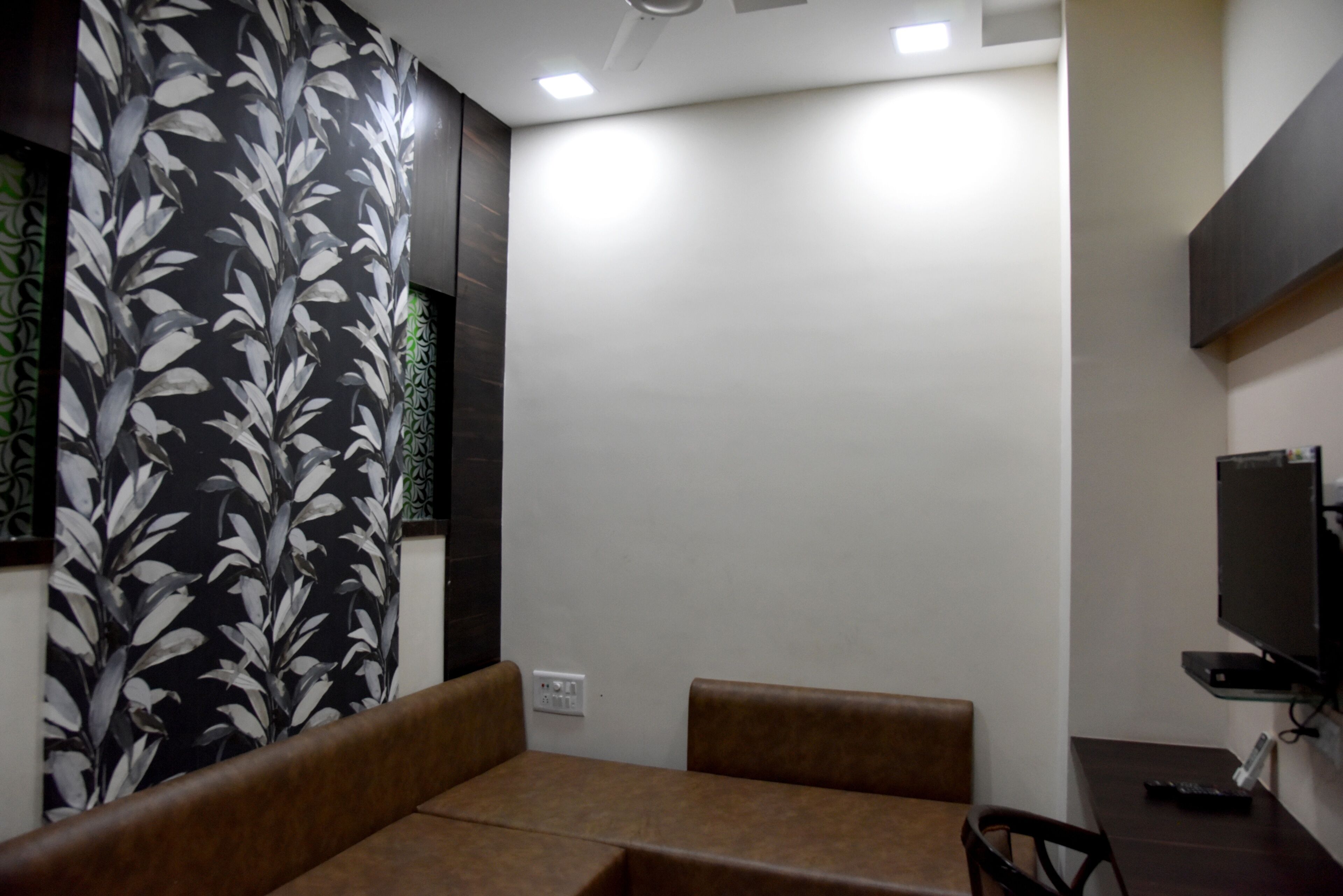 A modern room with a brown sofa, a flat-screen TV mounted on the wall, and a power outlet on the wall.