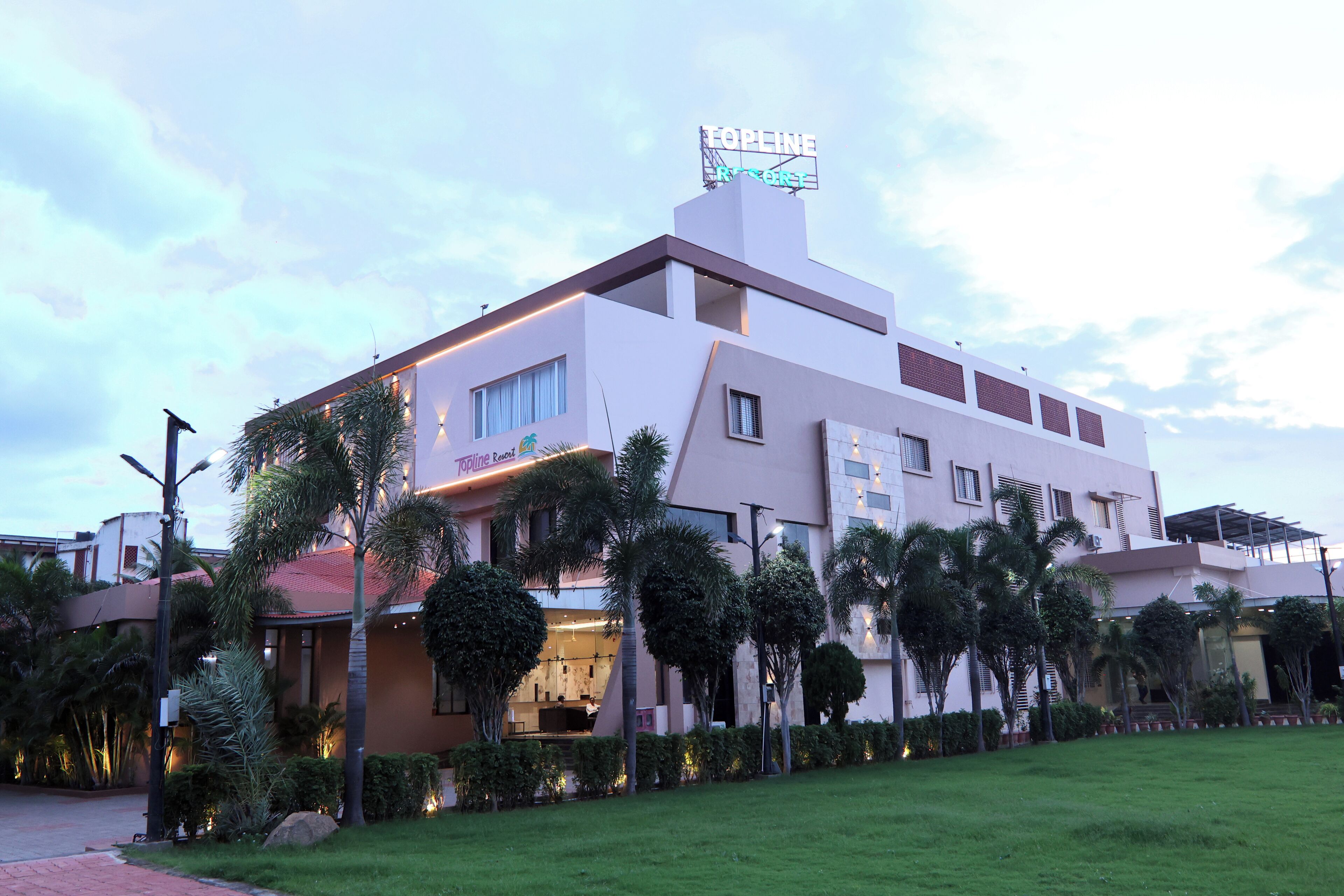 A modern hotel with a rooftop bar, palm trees, and a well-maintained lawn.