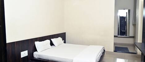 A modern hotel room with a large bed, a small seating area, a mirror, and an air conditioning unit.
