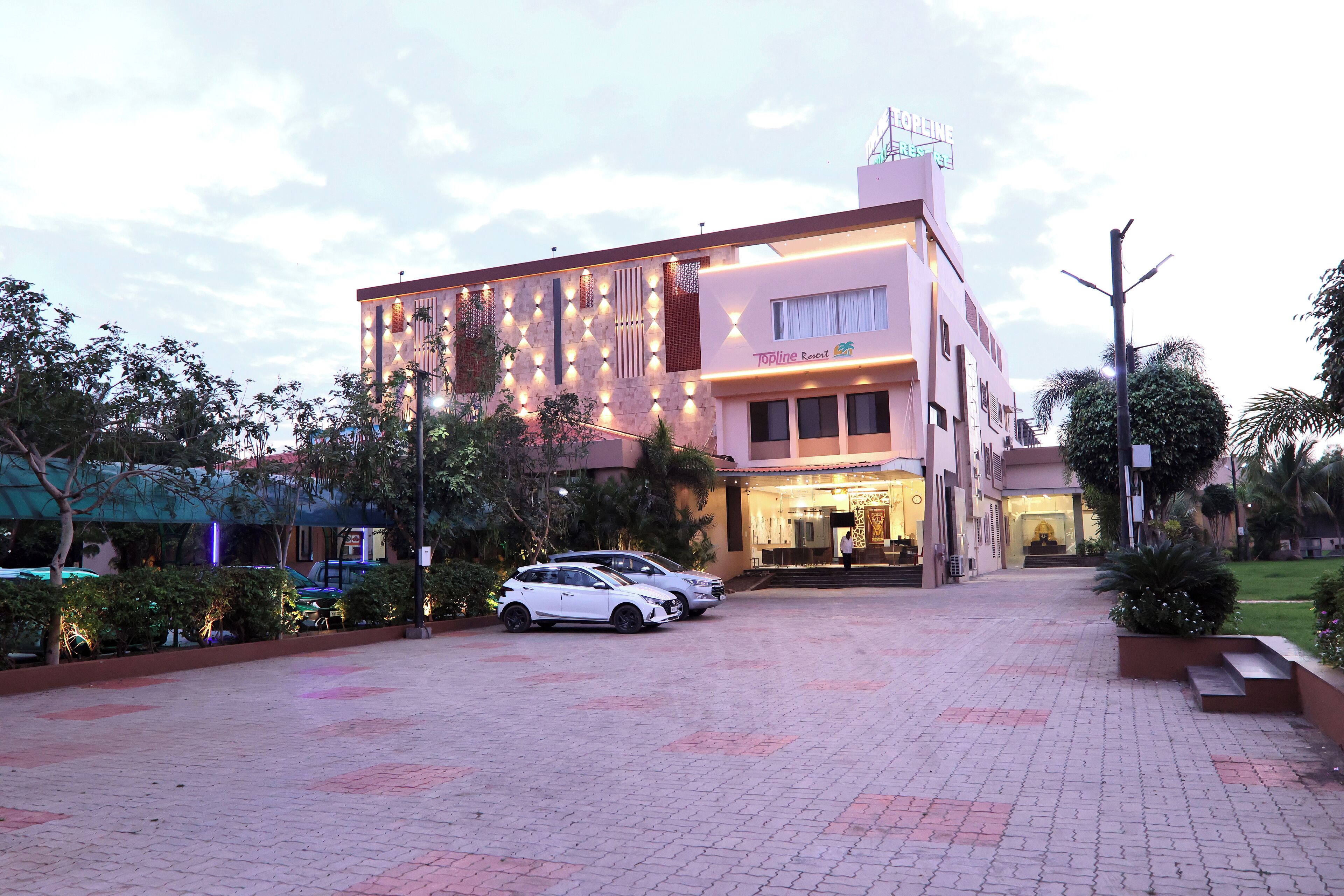 Un hotel con fachada moderna, un acceso bien iluminado y un camino pavimentado con coches aparcados.