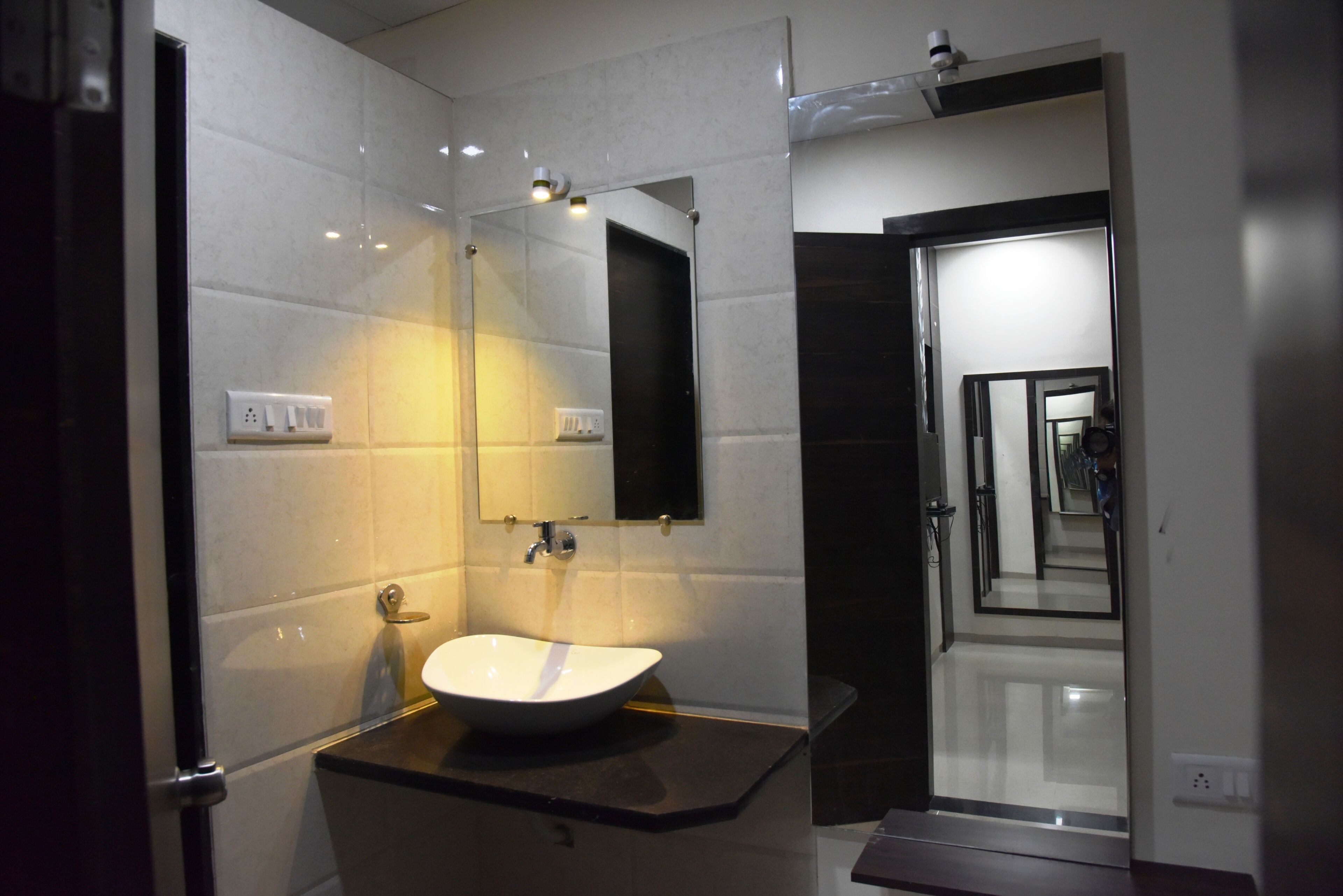 Une salle de bain moderne avec un lavabo blanc, un grand miroir et un plan de toilette foncé.