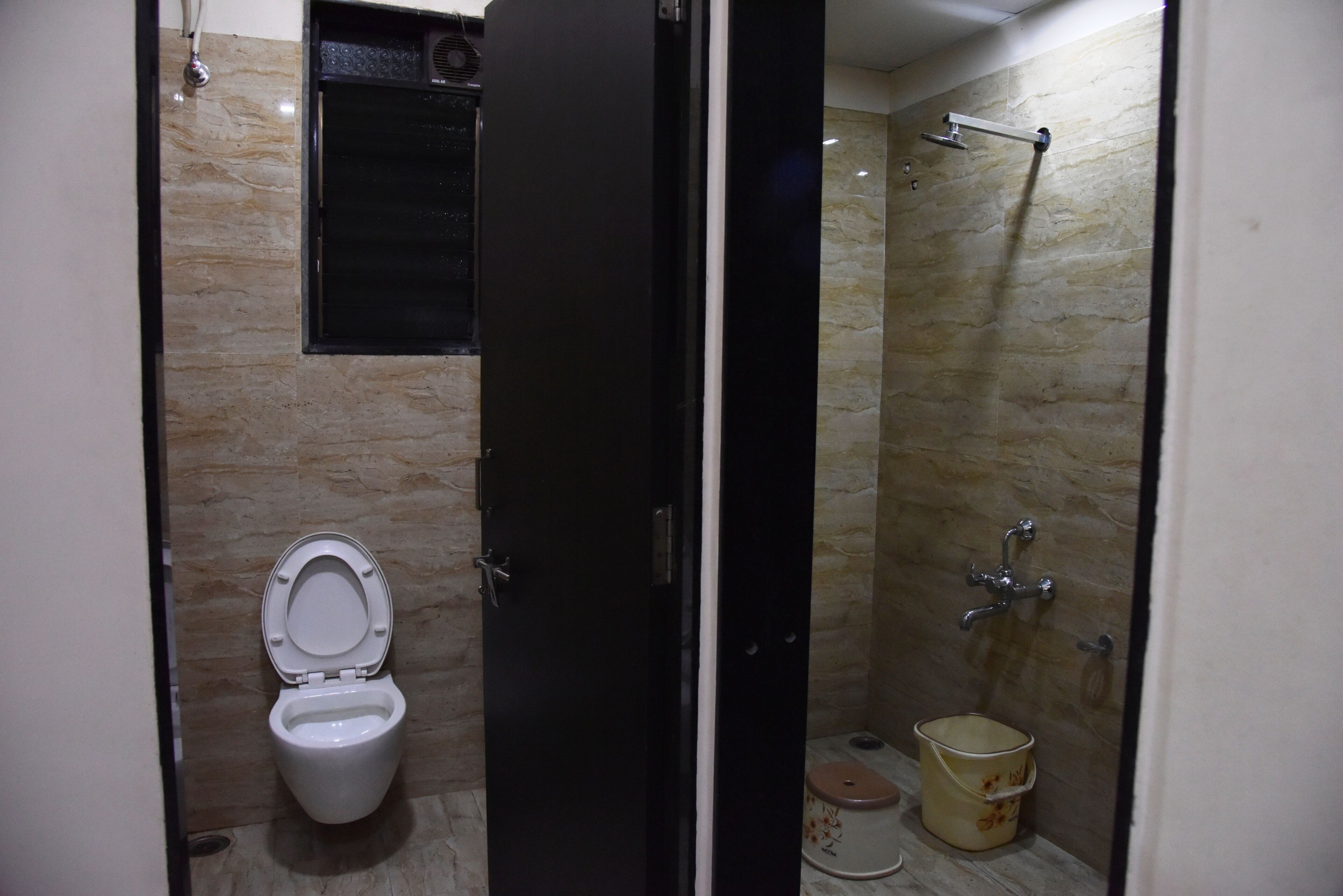 A small bathroom with a toilet, a shower, and a bucket.