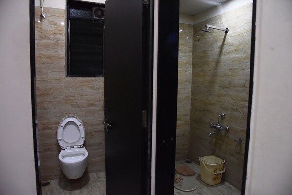 Une petite salle de bain avec des toilettes, une douche et un seau.