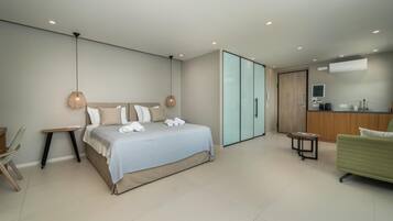 Un dormitorio moderno con una cama grande, un sofá verde, una mesita, un armario y una pequeña cocina.