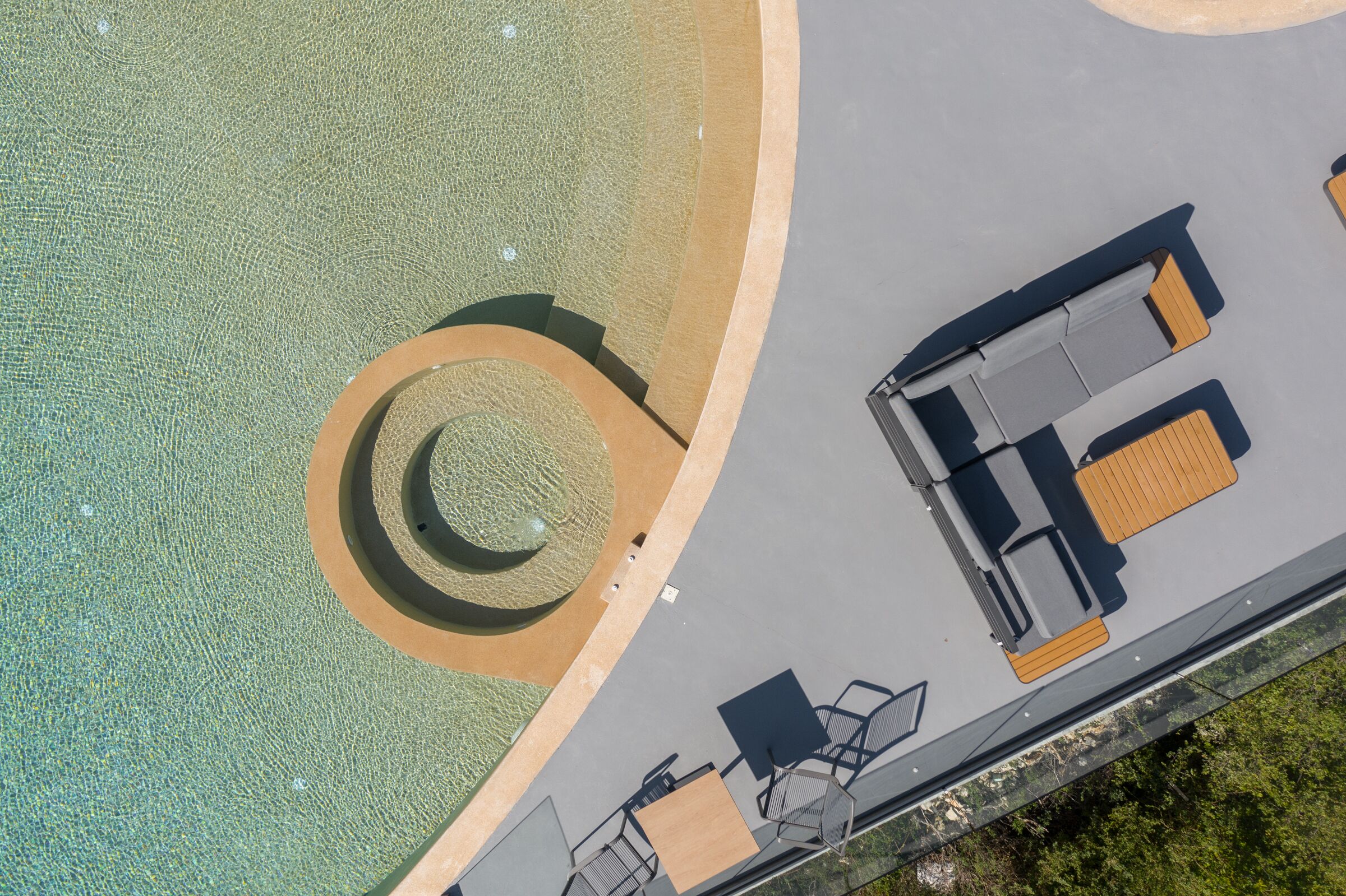 An aerial view of a pool area with a circular water feature, seating arrangements, and a pathway leading to the pool.