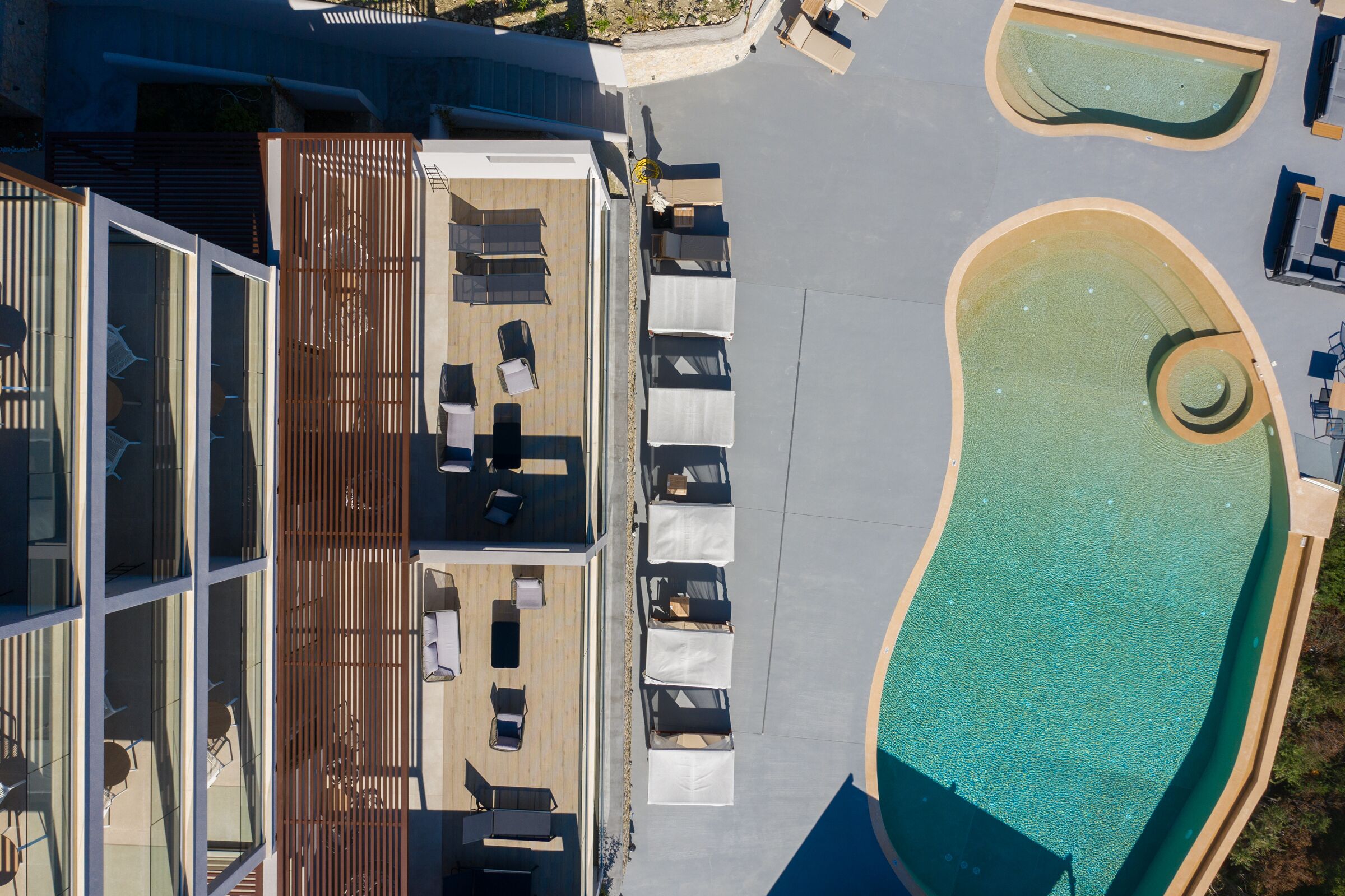 Vista aérea de una terraza en la azotea con tumbonas, una piscina y un área cerrada con vidrio que tiene mesas y sillas.