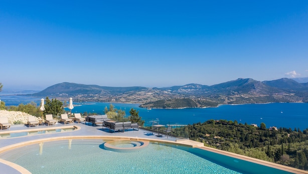 A pool area with lounge chairs and umbrellas, overlooking a scenic coastal landscape with mountains and a clear blue sea. - Katouna Suites Luxury Boutique Hotel - Adults Only (Lefkada)