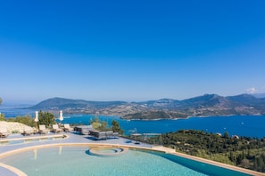 A pool area with lounge chairs and umbrellas, overlooking a scenic coastal landscape with mountains and a clear blue sea. - Katouna Suites Luxury Boutique Hotel - Adults Only (Lefkada)