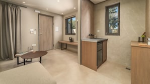 A modern, well-lit room with a wooden bench, a small table, and a kitchenette area. - Katouna Suites Luxury Boutique Hotel - Adults Only (Lefkada)