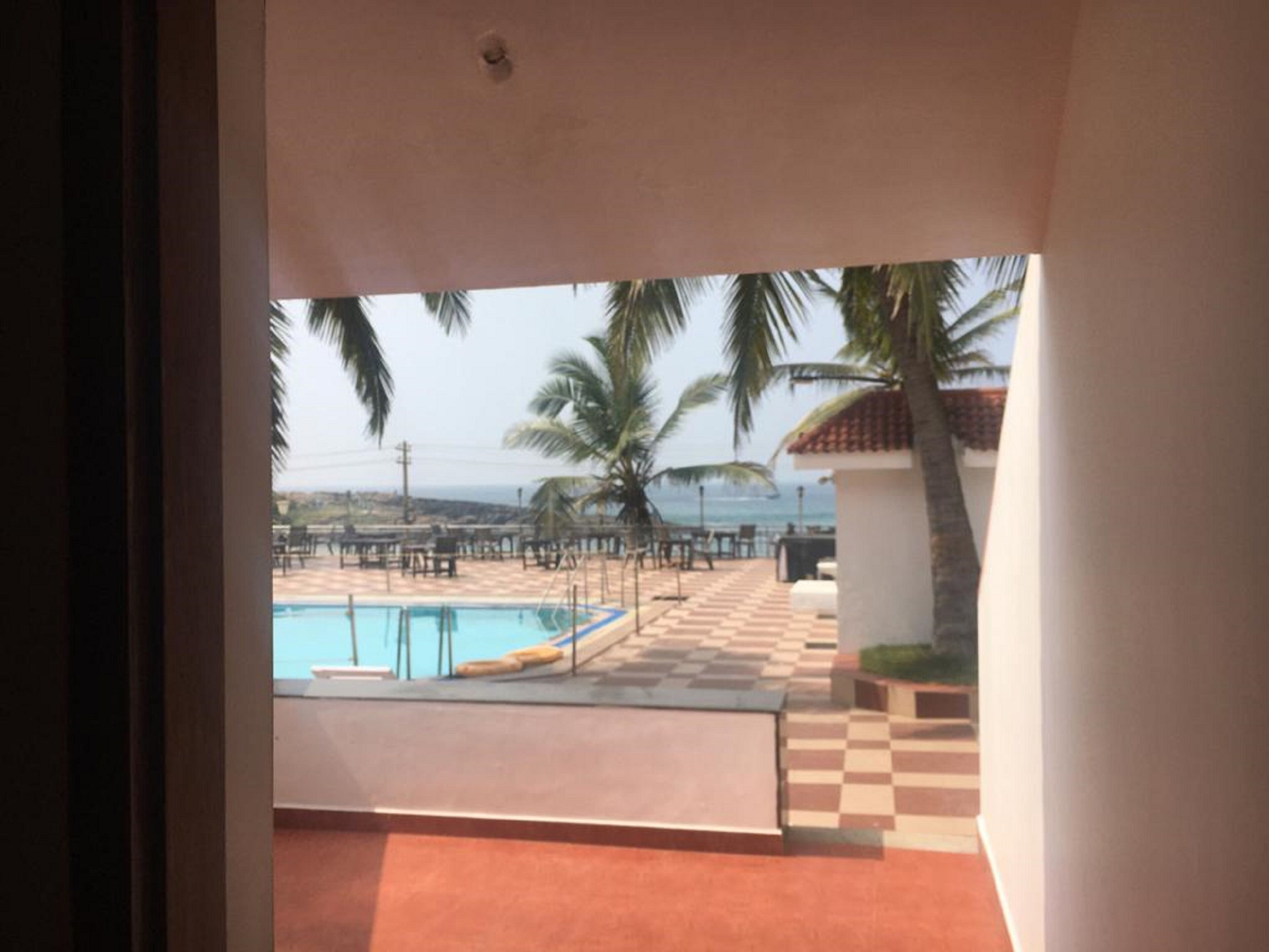 Vista di una piscina con bordo piastrellato, palme e, sullo sfondo, il mare.