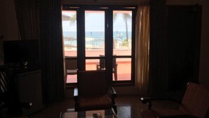 A room with a television, a sofa, a coffee table, and a view of the beach through the sliding glass door. - Hotel Sea Face (Neyyattinkara)