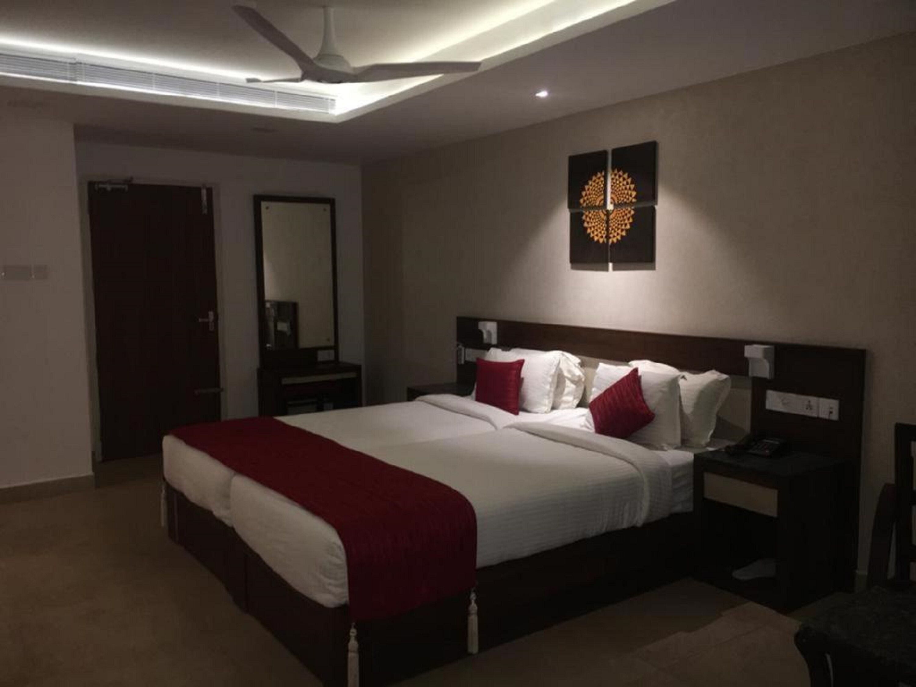 Ein Hotelzimmer mit einem großen Bett, einem Nachttisch, einem Spiegel und einem Deckenventilator.