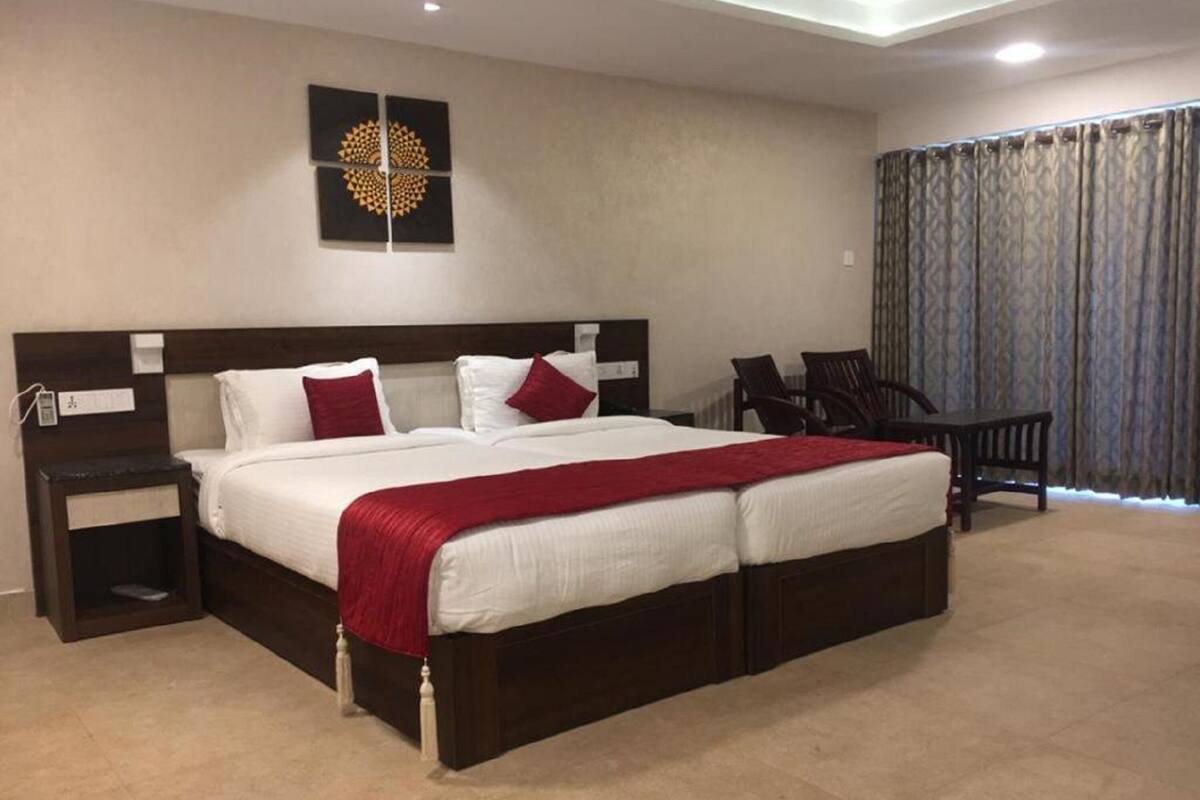 A double bed with a red throw, two bedside tables, a wall art piece, and a view of the outside through curtains.