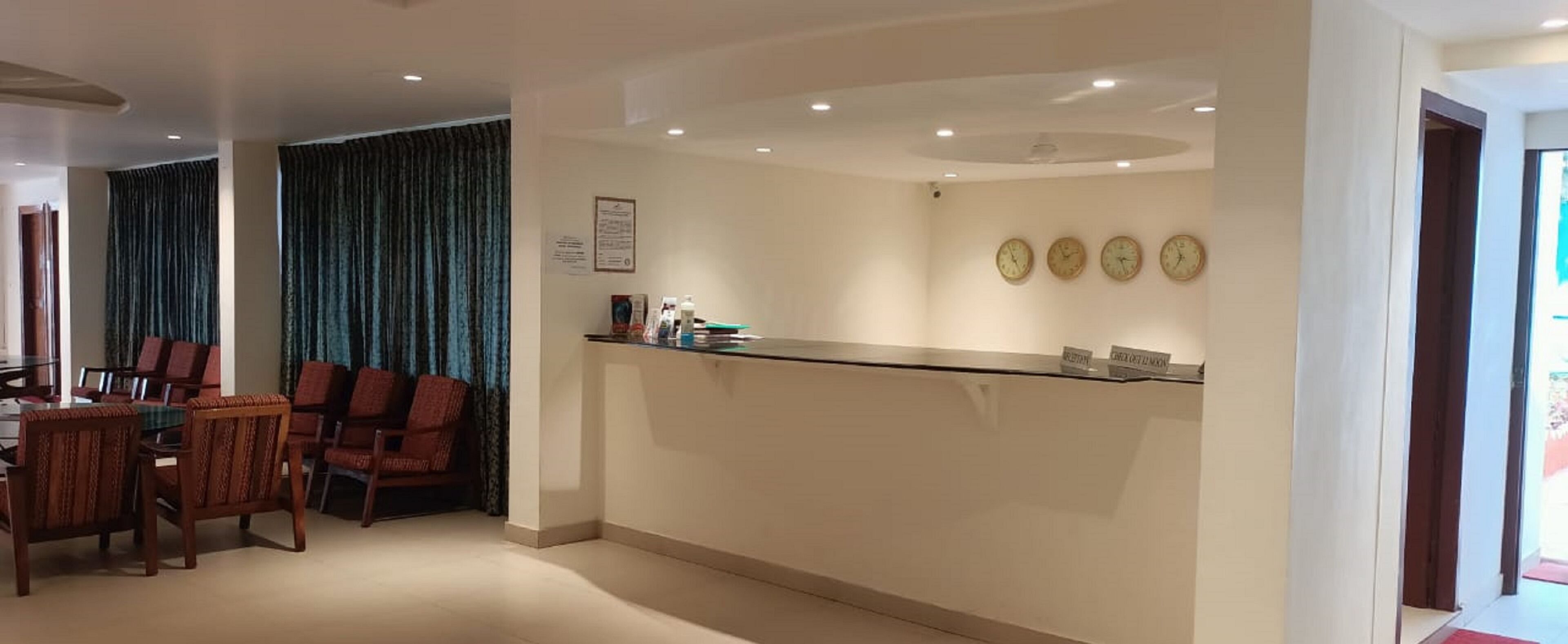 A hotel lobby with a reception desk, a dining area with chairs and a table, and a wall with clocks.