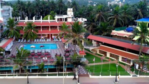 A hotel with a swimming pool, palm trees, and a red-roofed building. - Hotel Sea Face (Neyyattinkara)