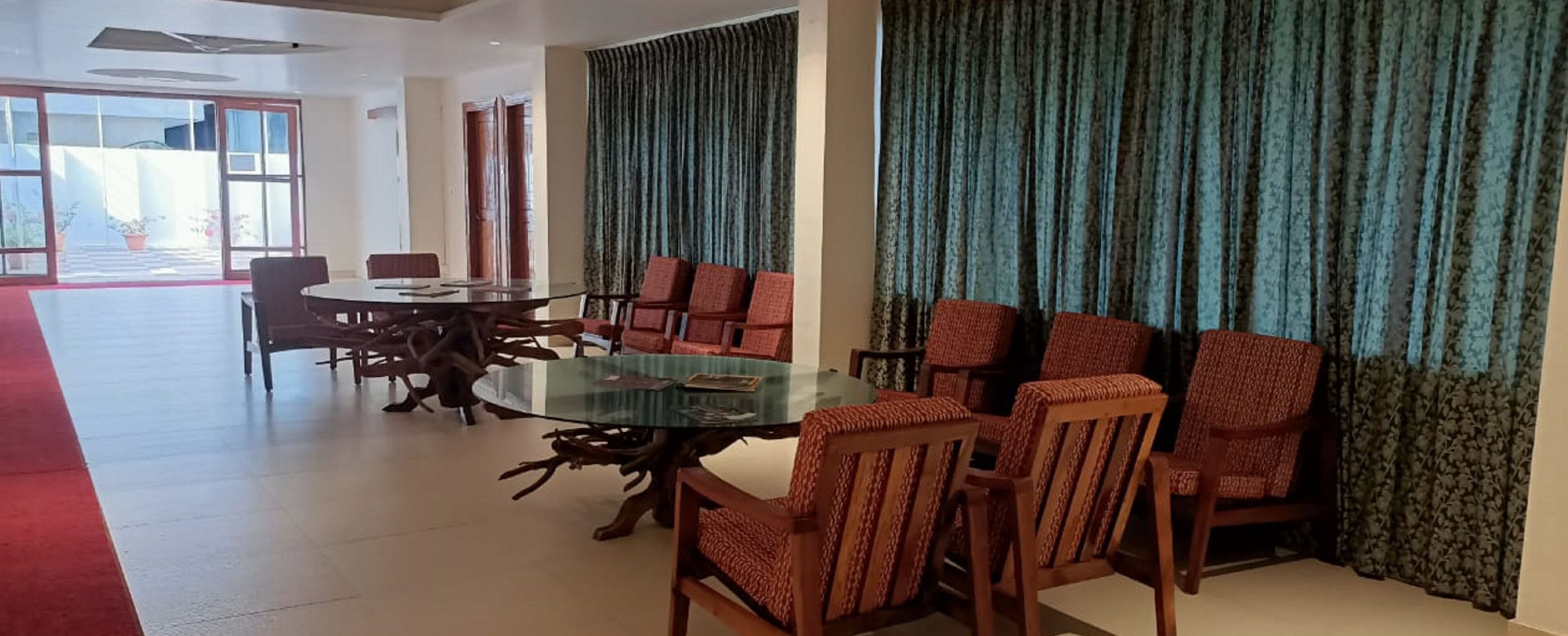 A conference room with a glass table surrounded by wooden chairs, a red carpet, and large windows with curtains.