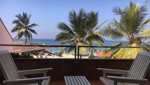 A balcony with two white lounge chairs and a small table, overlooking a beach with palm trees and the ocean. - Hotel Sea Face (Neyyattinkara)